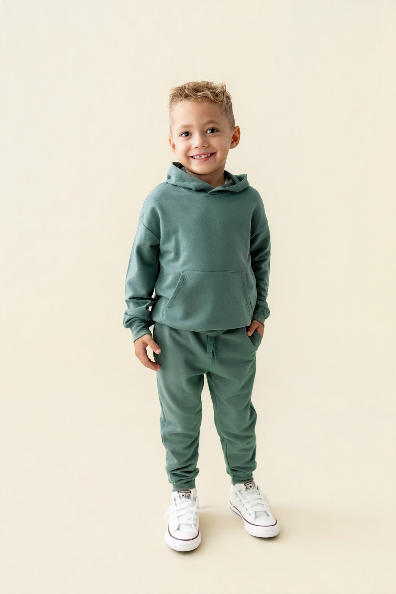 Boy posing in Hoodie in Pine color and pine color jogger pants on a beige background