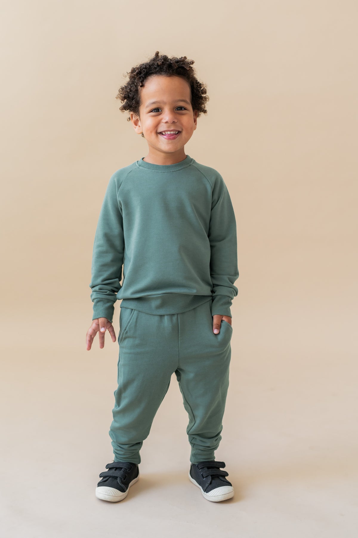 Boy posing in Long Sleeve Jogger Set in Pine color on a beige background