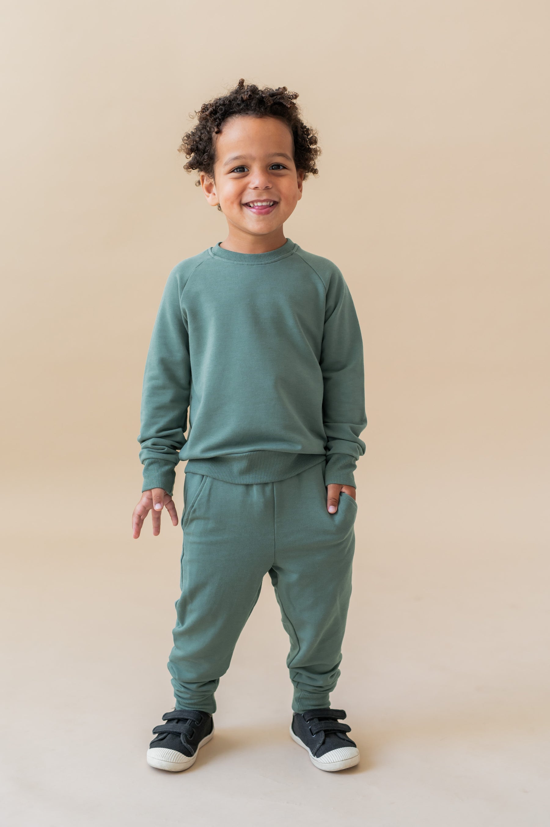 Boy posing in Long Sleeve Jogger Set in Pine color on a beige background