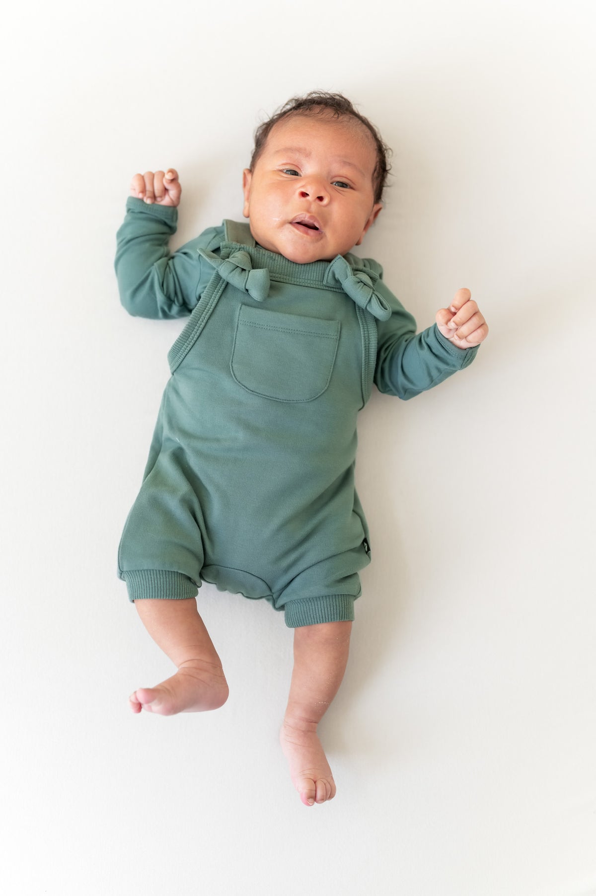 Baby wearing Overall in Pine color over similar color shirt  on a beige background