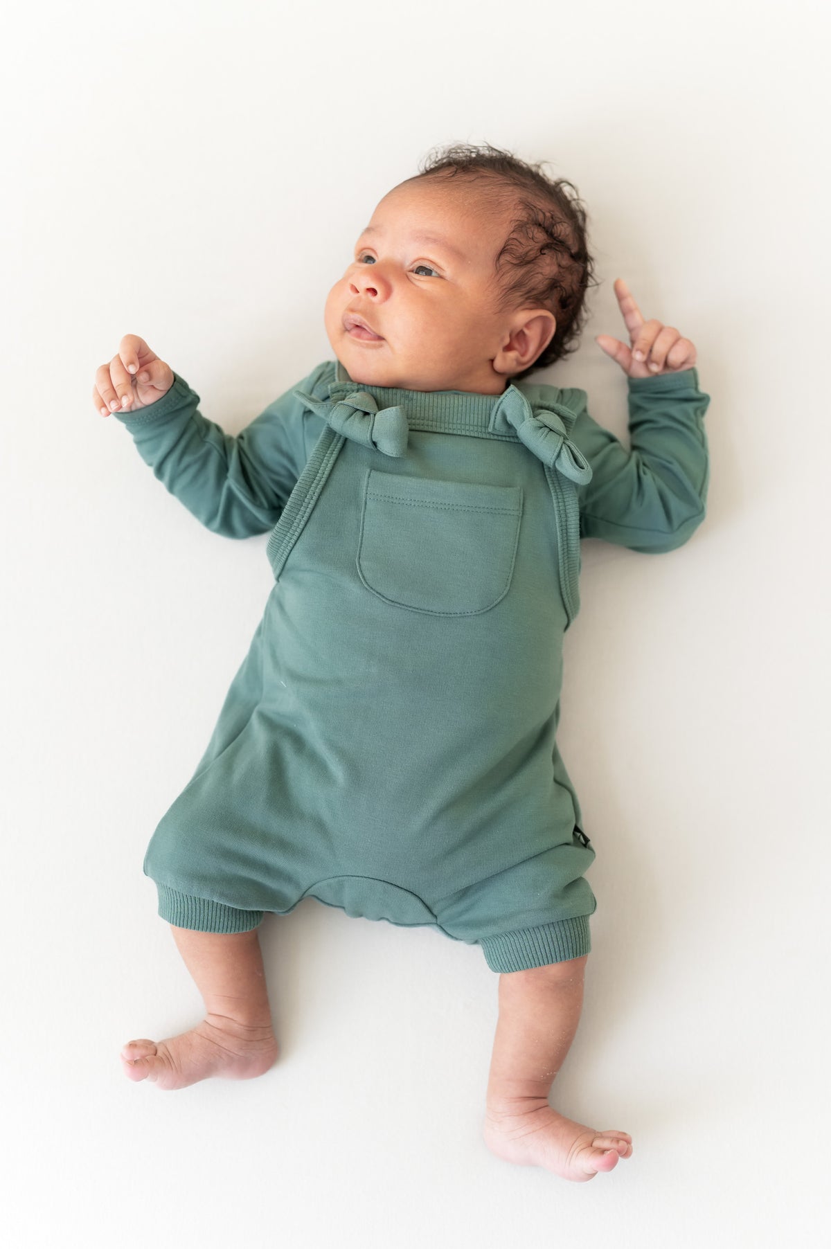 Baby wearing Overall in Pine color over similar color shirt lying on a beige background
