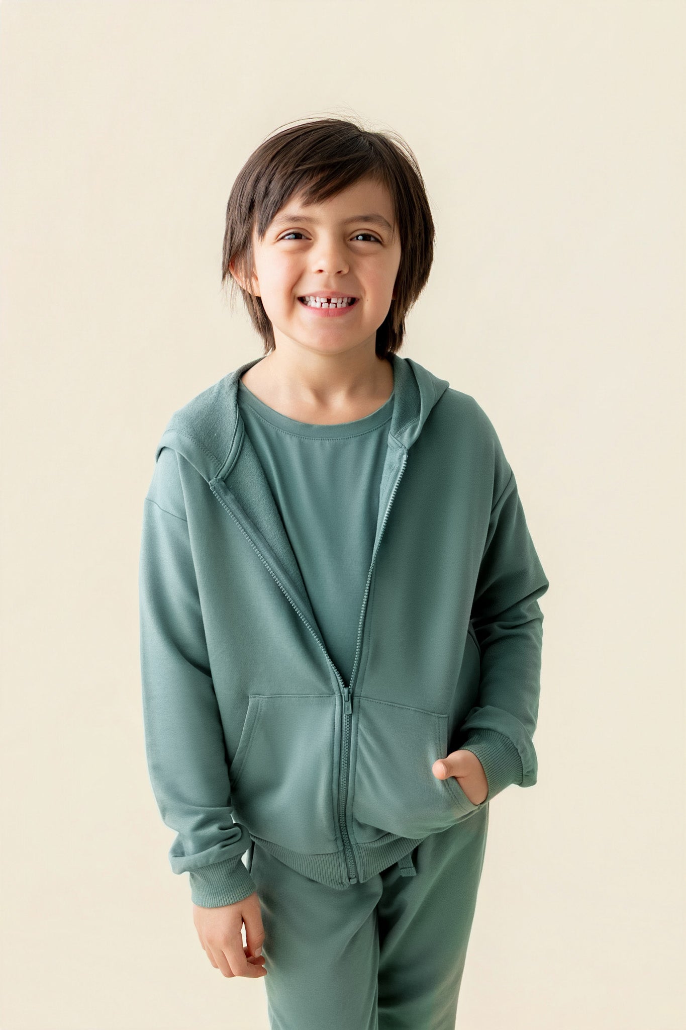 Boy smiling in Zip-Up Hoodie in Pine color over similar color jogger pant on a beige background