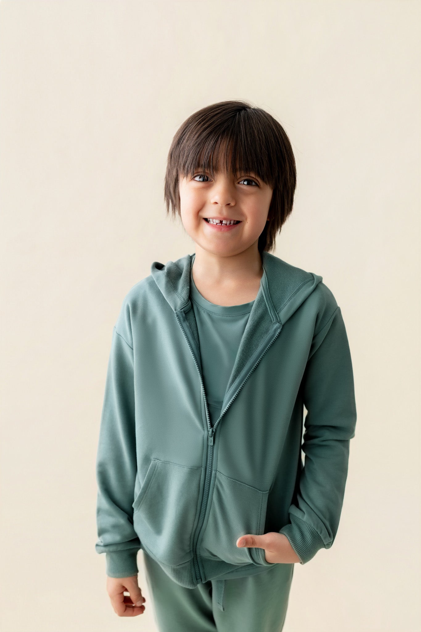 Boy posing in Zip-Up Hoodie in Pine color with pockets over similar color jogger pant on a beige background
