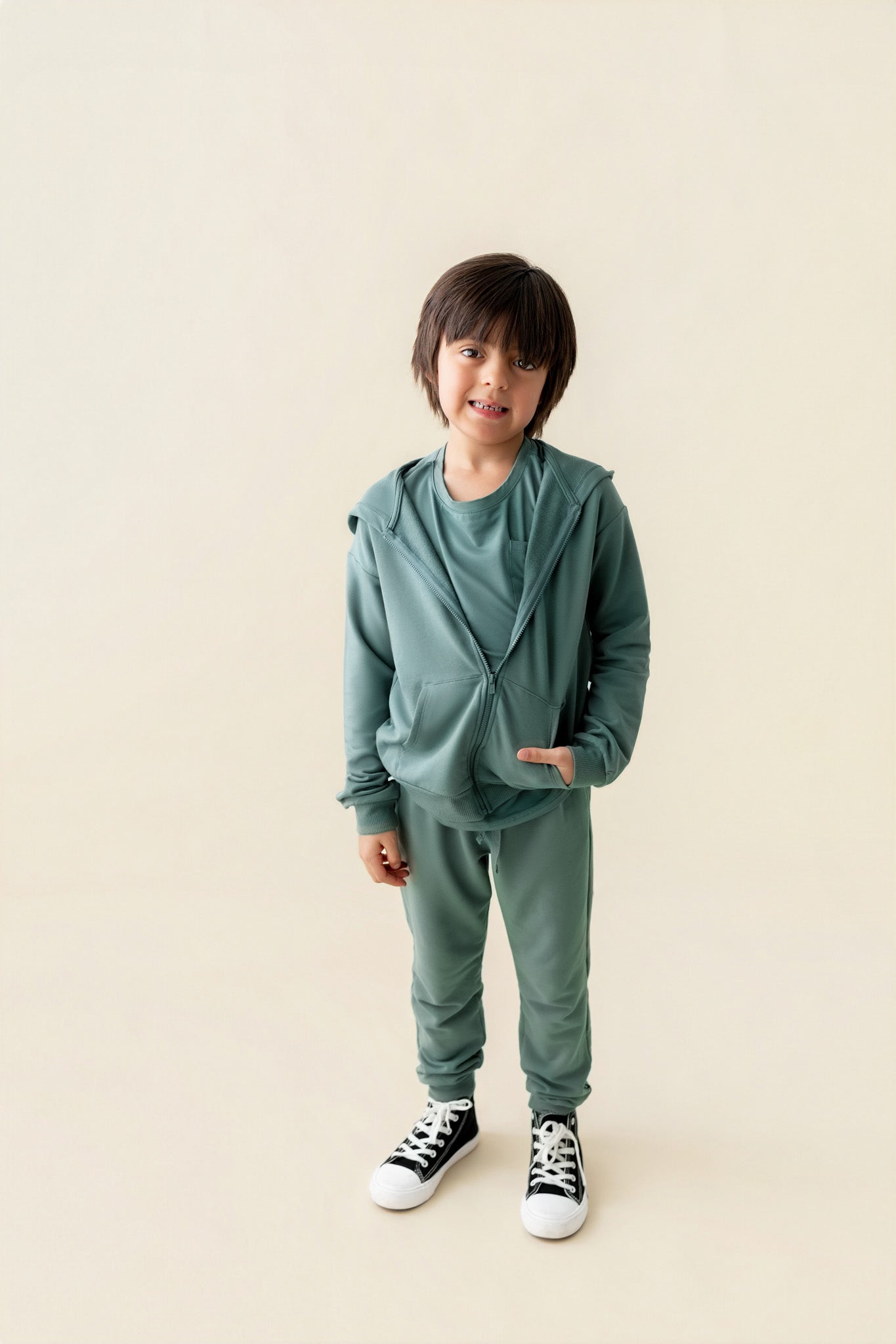 Boy wearing Jogger Pant in Pine color under pine color Zip up hoodie on a beige background