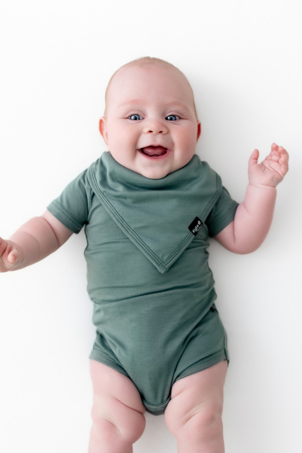 Baby smiling wearing Bib in Pine over similar color bodysuit on a white background