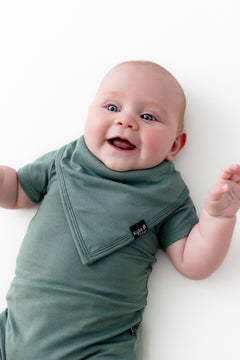 Baby wearing Bib in Pine over similar color bodysuit on a white background