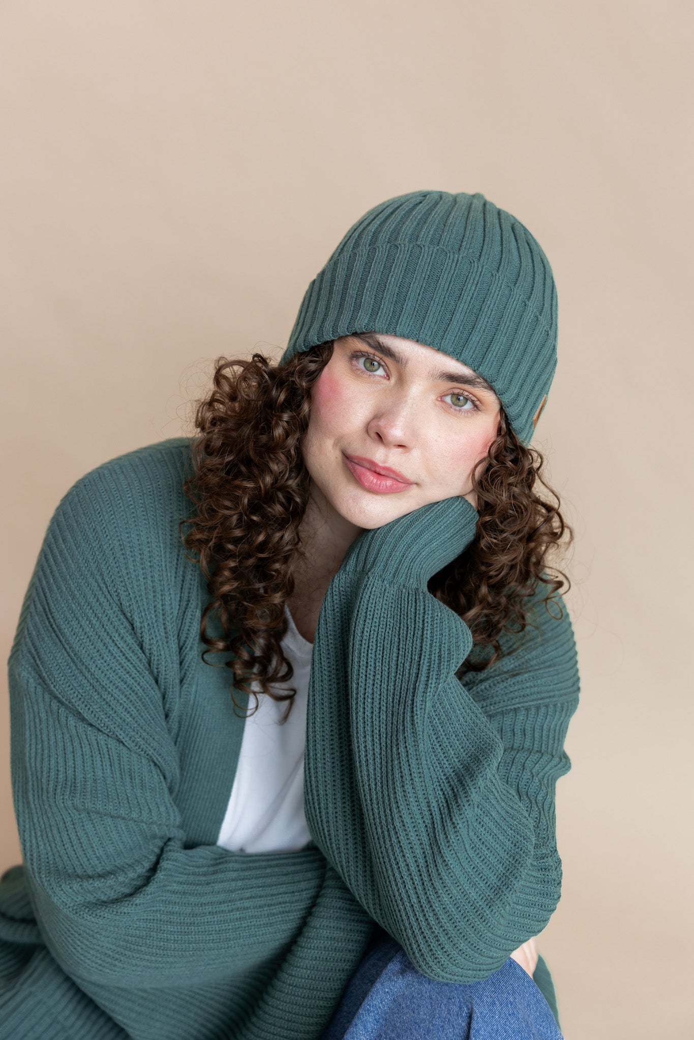 Modal wearing Chunky Knit Adult Ribbed Beanie in Pine over white T-shirt and Chunky knit cardigan in Pine on a beige background