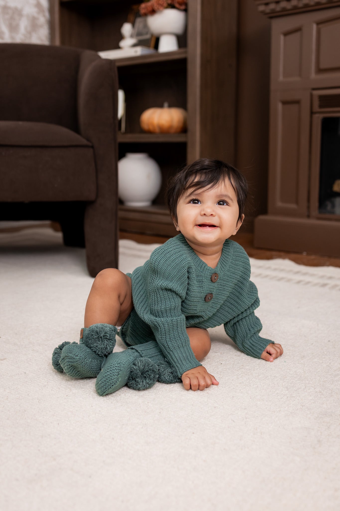 Baby wearing Chunky Knit Romper and knit booties in Pine on a white carpet