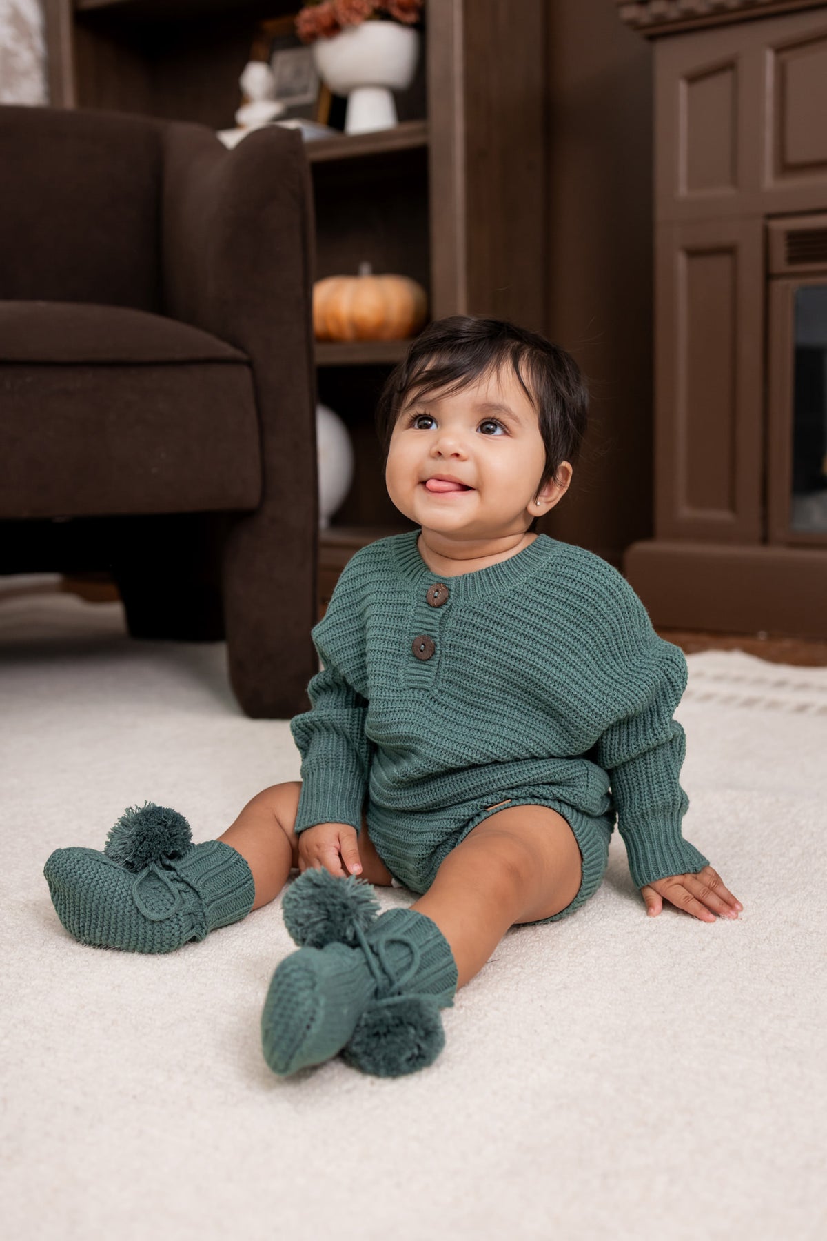 Baby sitting on white carpet while wearing Chunky Knit Romper and knit booties in Pine
