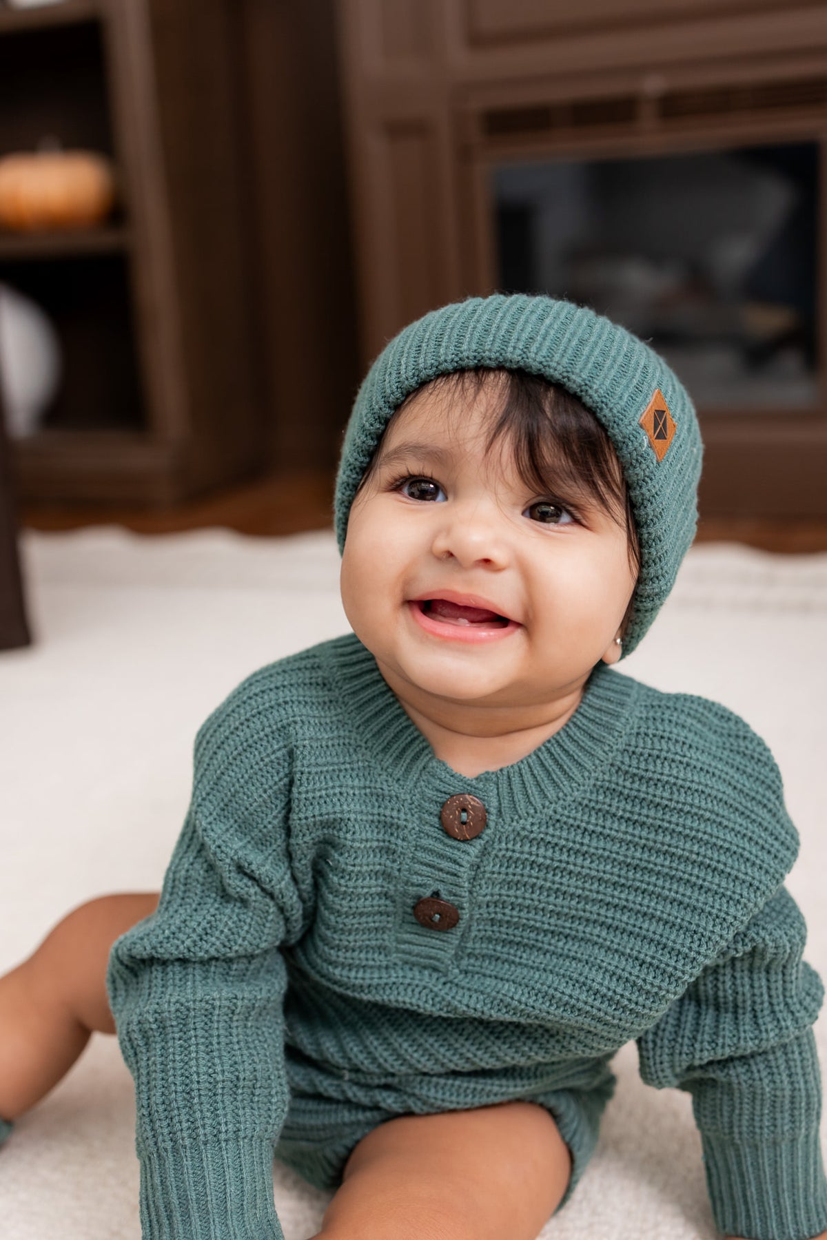 Baby wearing Chunky Knit Pom Beanie in Pine over chunky knit romper on white carpet