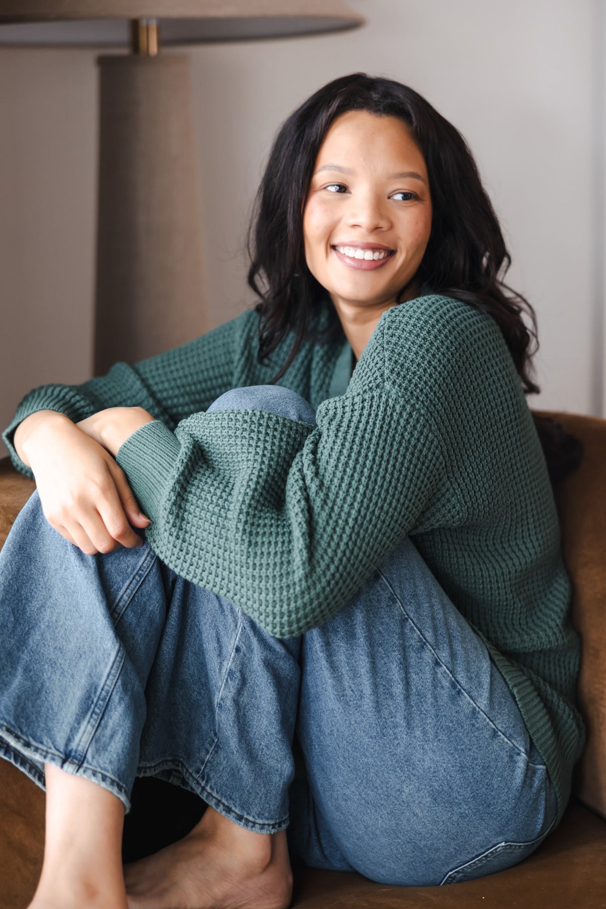 Modal smiling while wearing Chunky Knit Women's Waffle Cardigan in Pine over blue jeans 