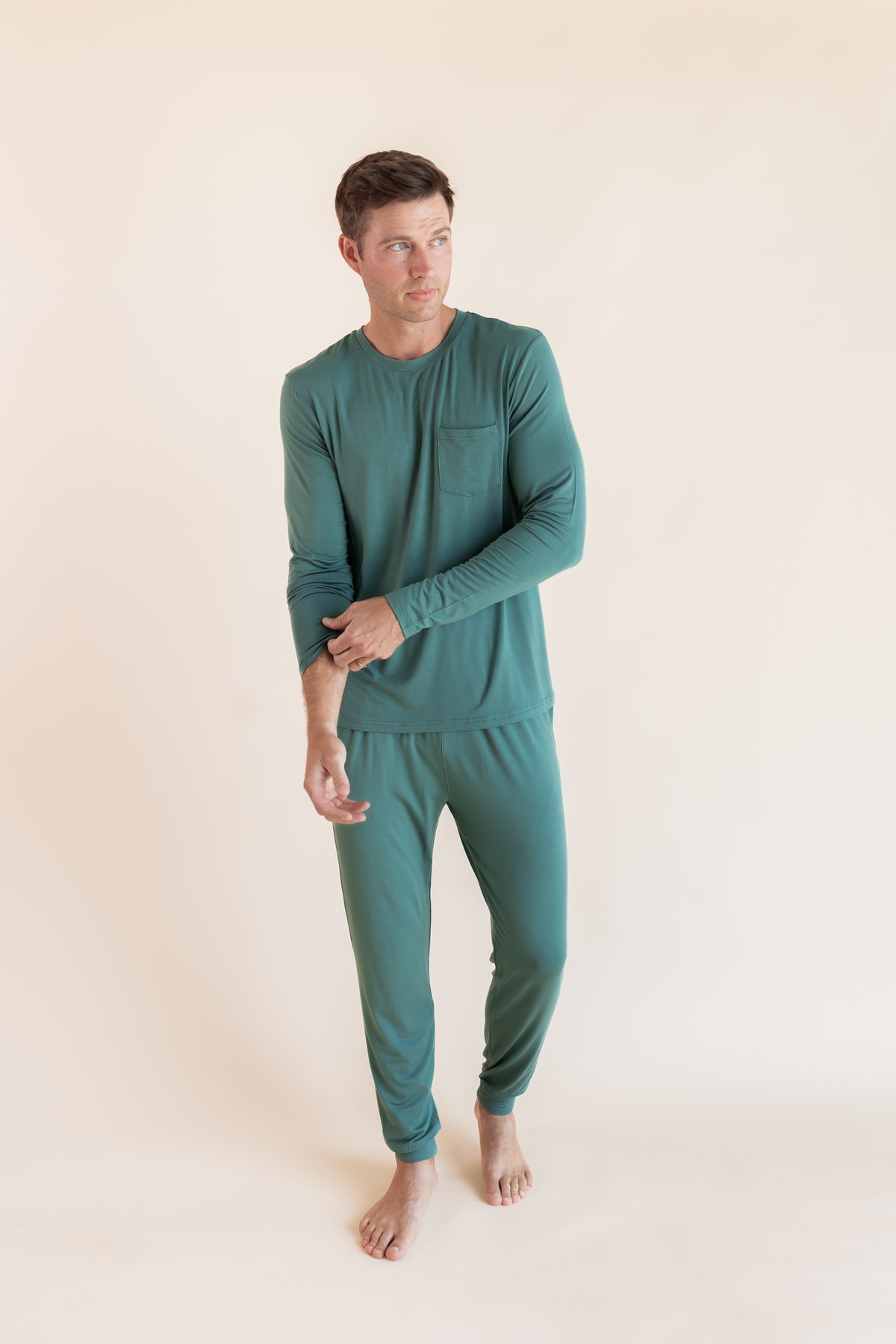 Model posing in Men's Jogger Set in Pine on a beige background