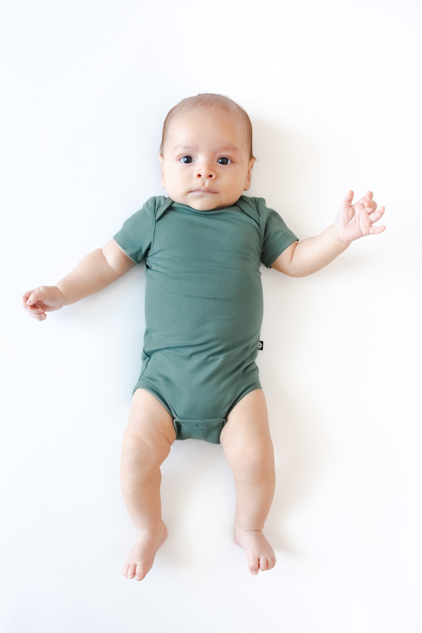 A baby lying on their back wearing a muted sage green short-sleeve bodysuit