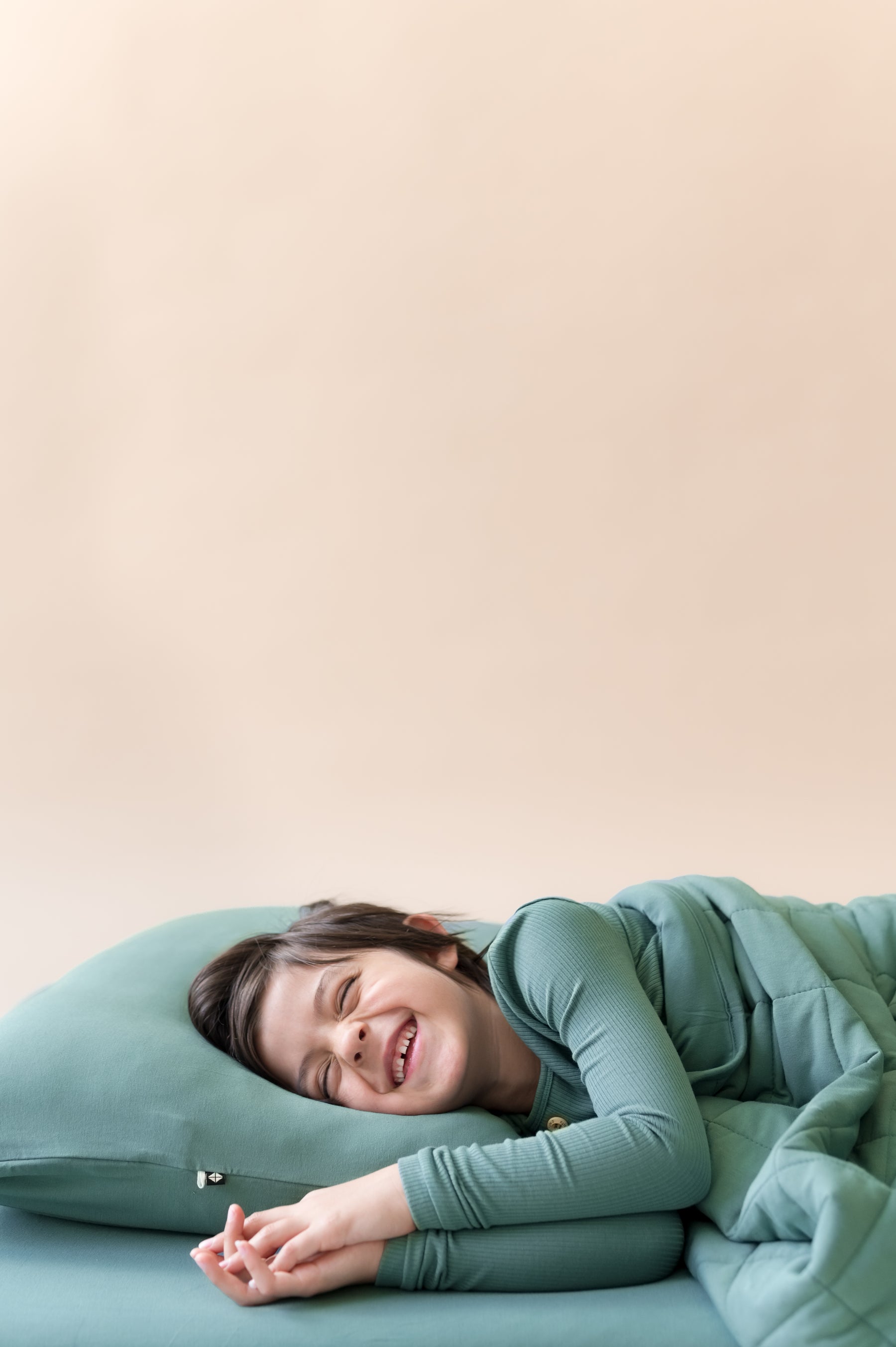 Boy lying on Standard Pillowcase in Pine over a bed with pine sheet and wearing pine shirt covered with pine blanket