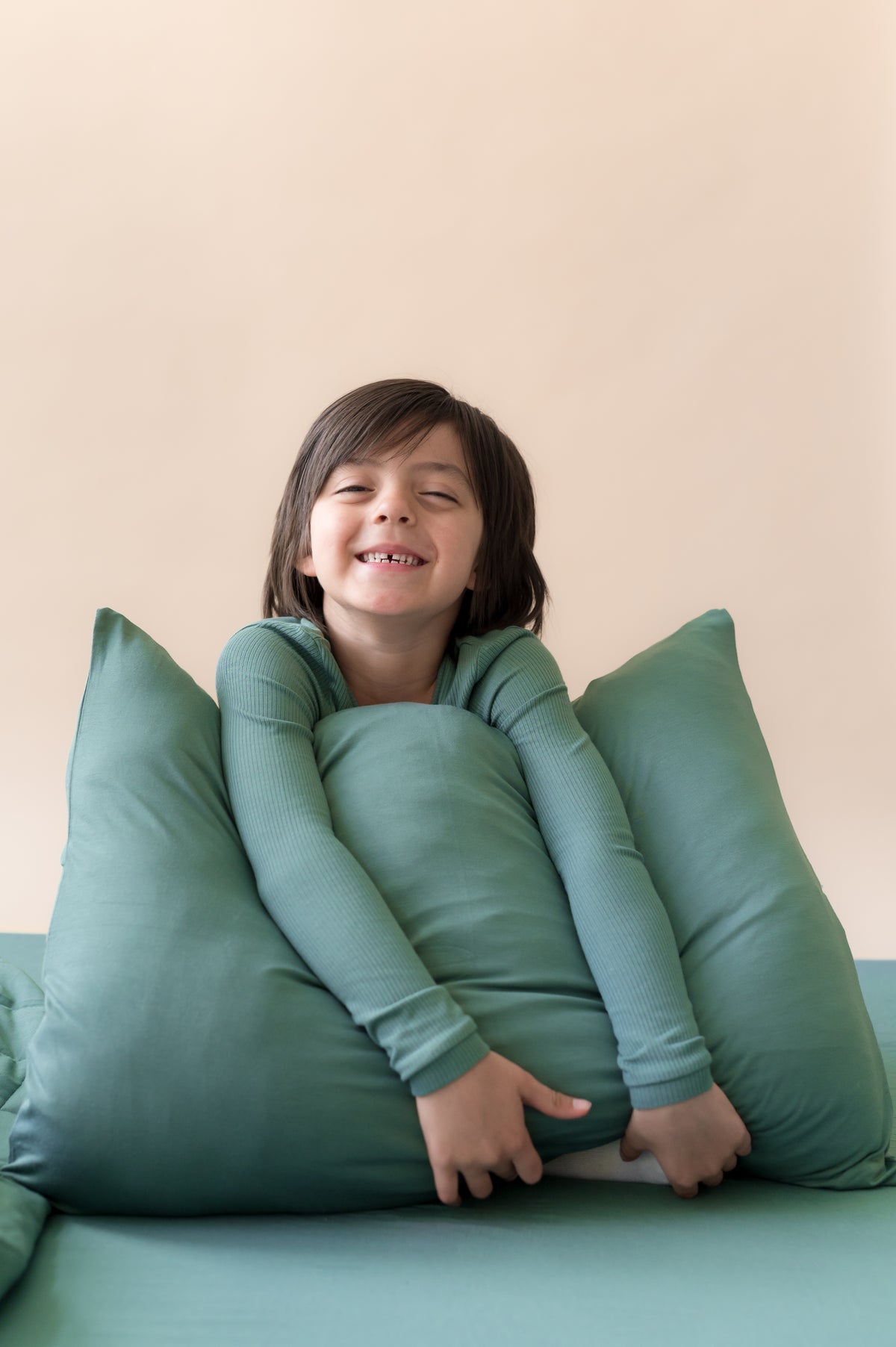 Boy holding Standard Pillowcase in Pine sitting on a bed with pine sheet and wearing pine shirt