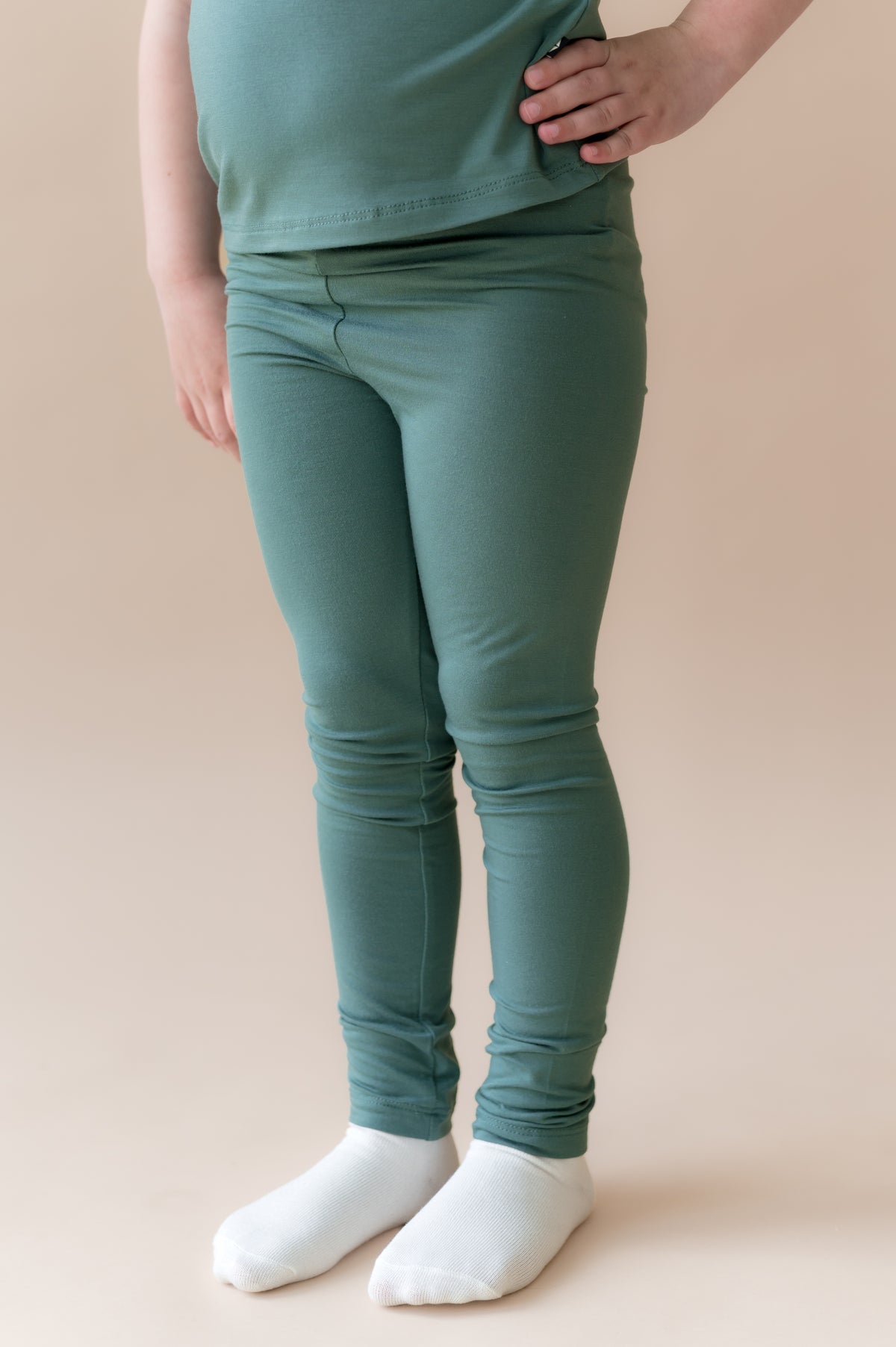 Child wearing Toddler Leggings in Pine under pine shirt on a beige background