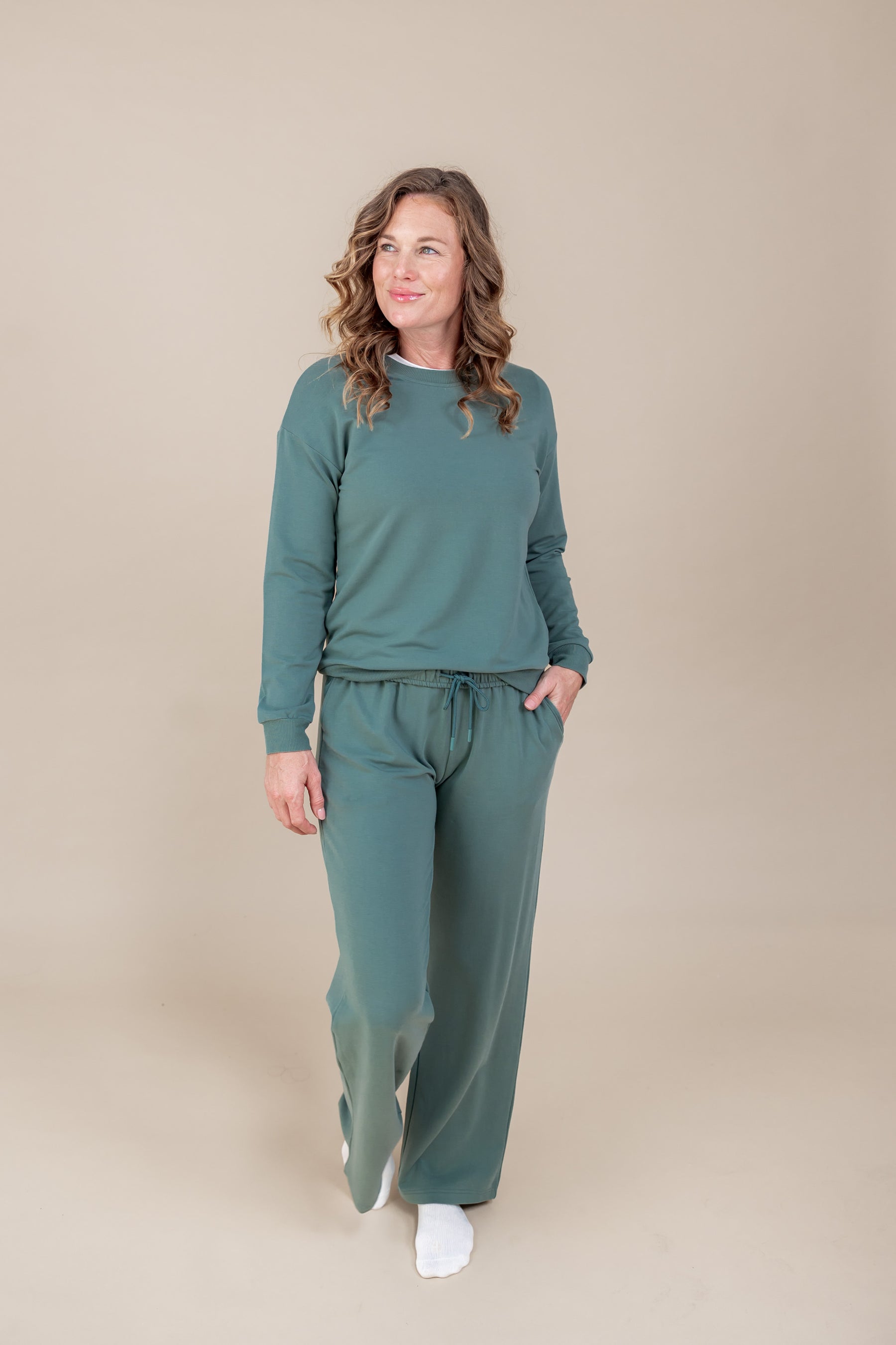 Woman posing in Women's Sweatshirt in Pine color over Women's sweatpants in pine on a beige background