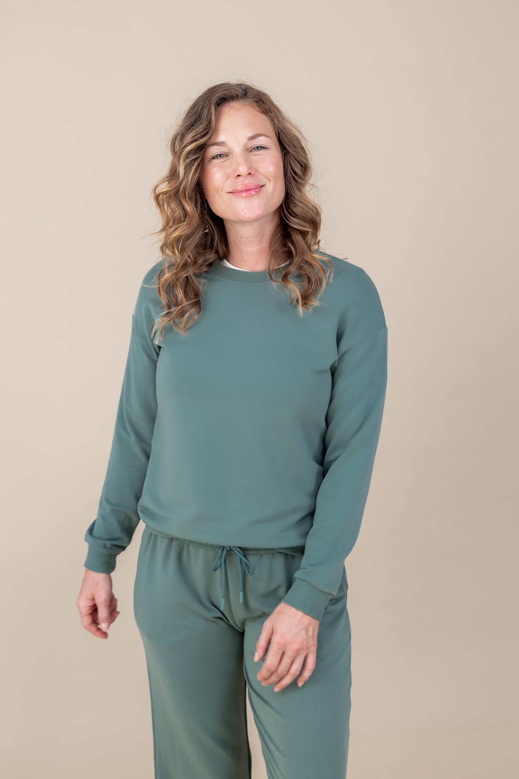 Woman wearing Women's Sweatshirt in Pine color over Women's sweatpants in pine on a beige background