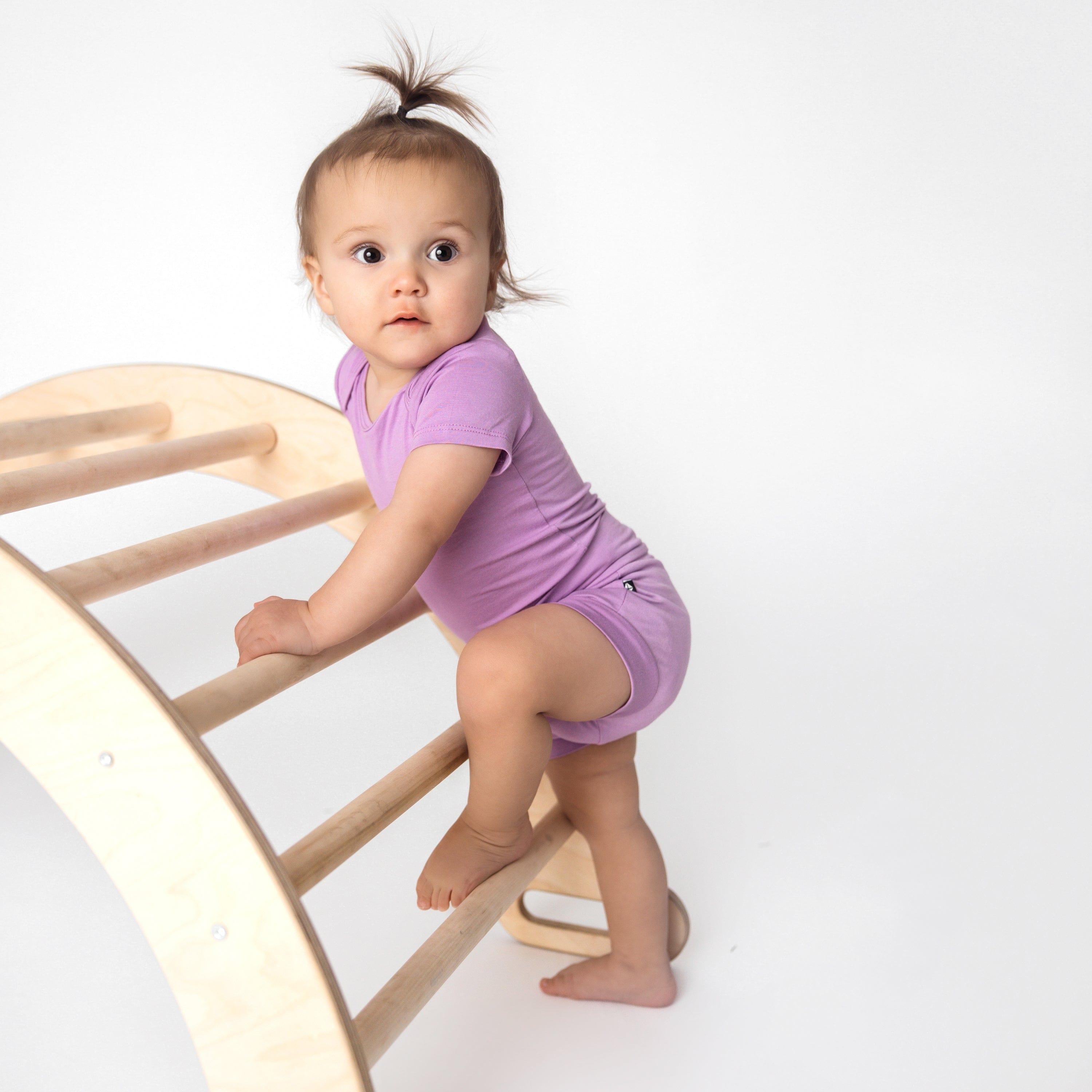 toddler wearing bodysuit and bummies in poi climbing on a toy