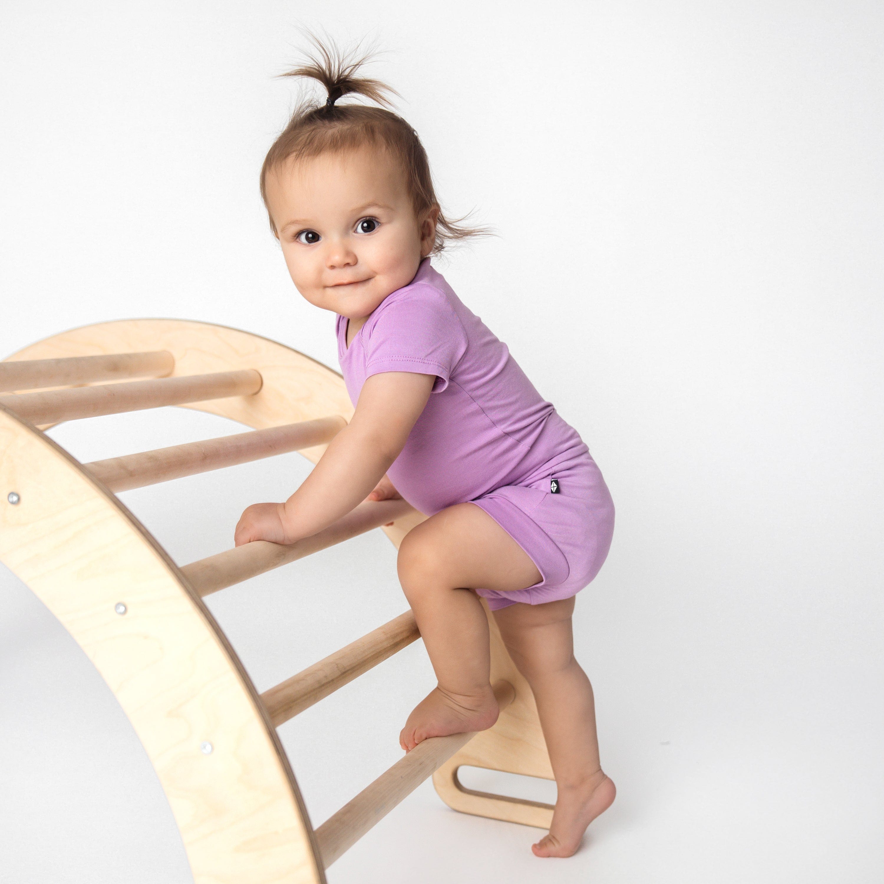 toddler wearing bodysuit and bummies in poi climbing on a toy