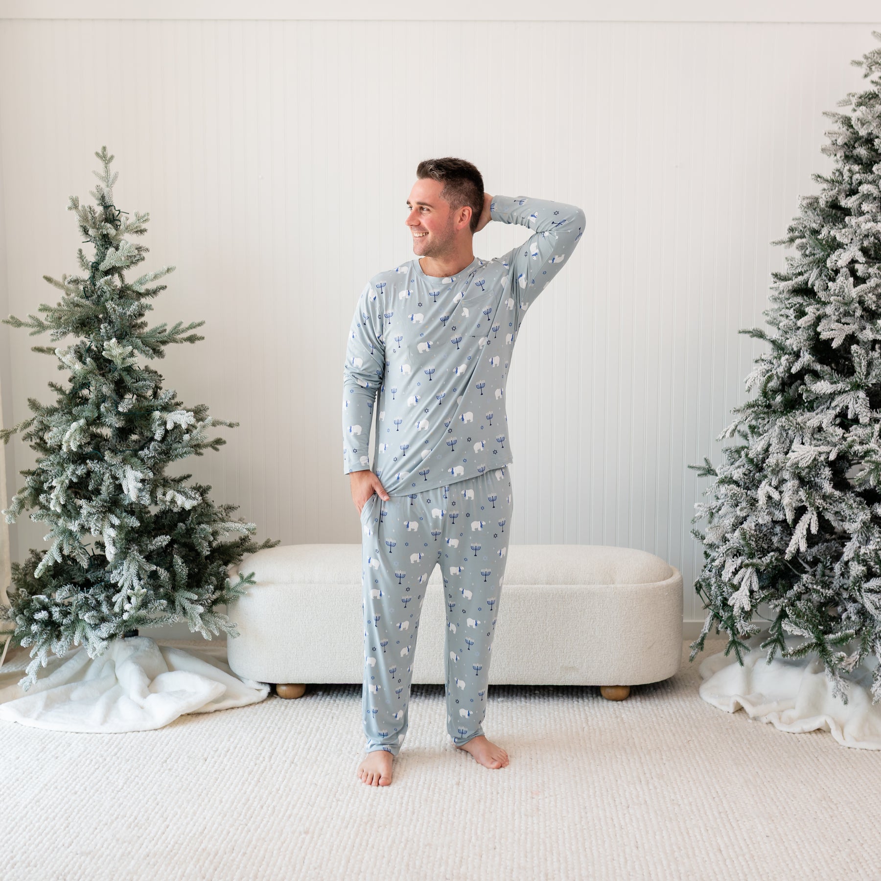 Male model standing between two frosted trees wearing the Men's Jogger Set in Polar Lights with one hand in pants pocket and the other behind his head