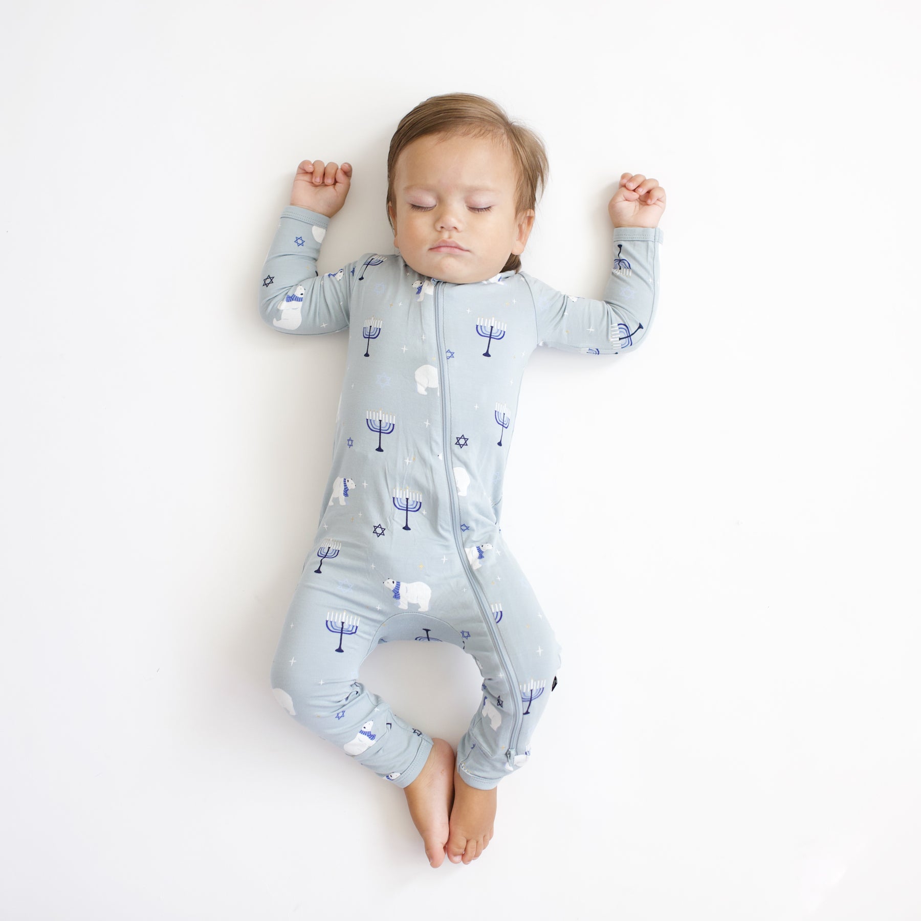 Sleeping infant laying on a white blanket wearing the Zippered Romper in Polar Lights