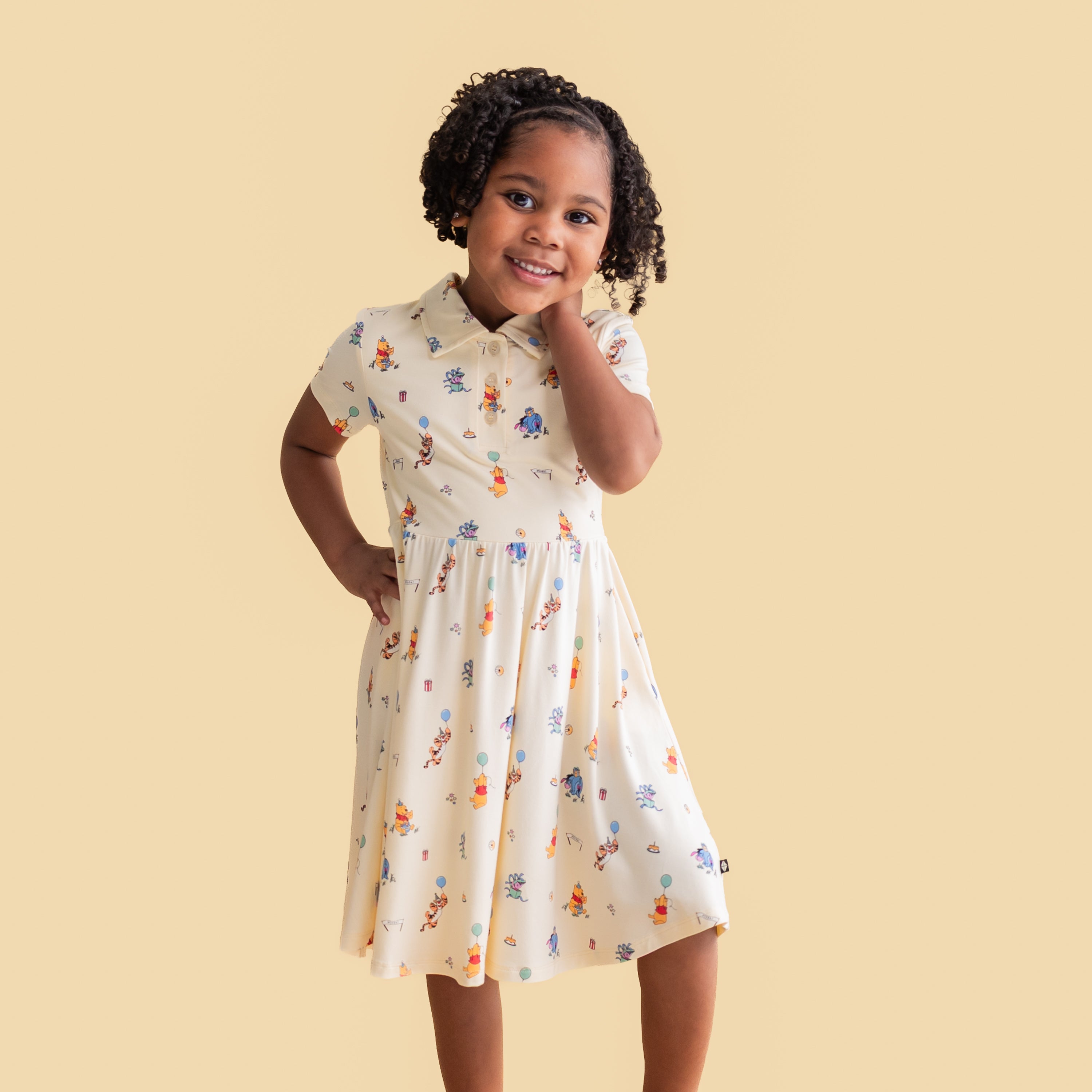 Young girl posing wearing the Polo Dress in Winnie the Pooh Celebration in front of a yellow background