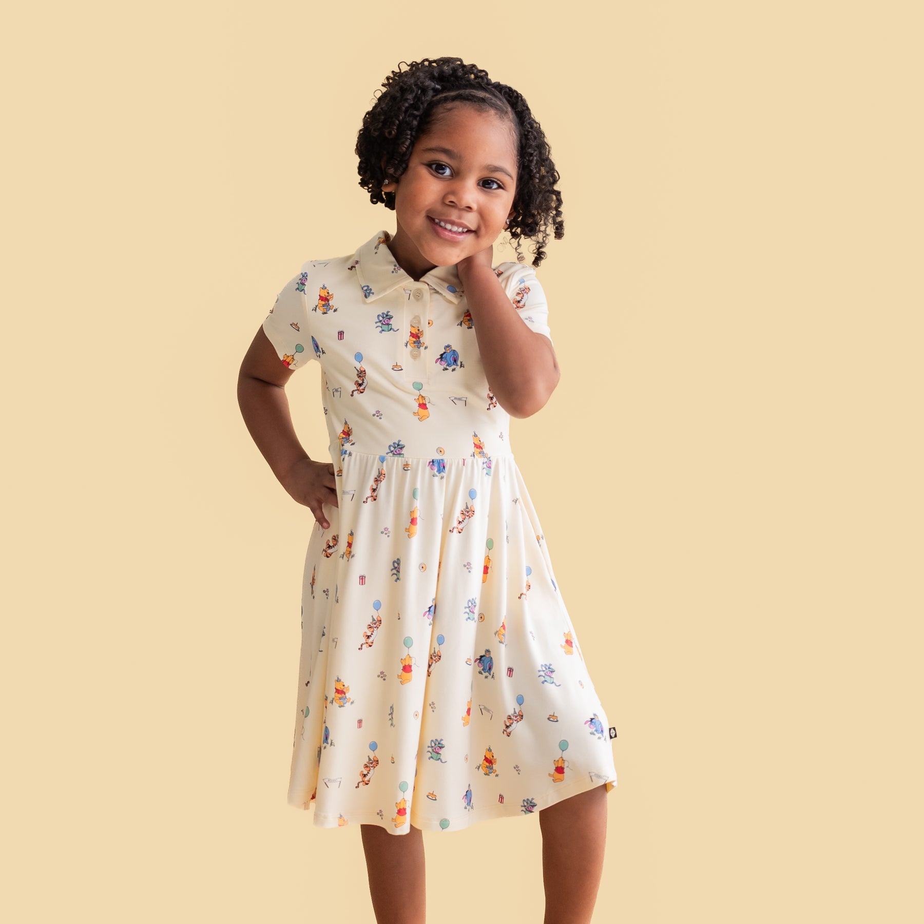 Young girl posing wearing the Polo Dress in Winnie the Pooh Celebration in front of a yellow background