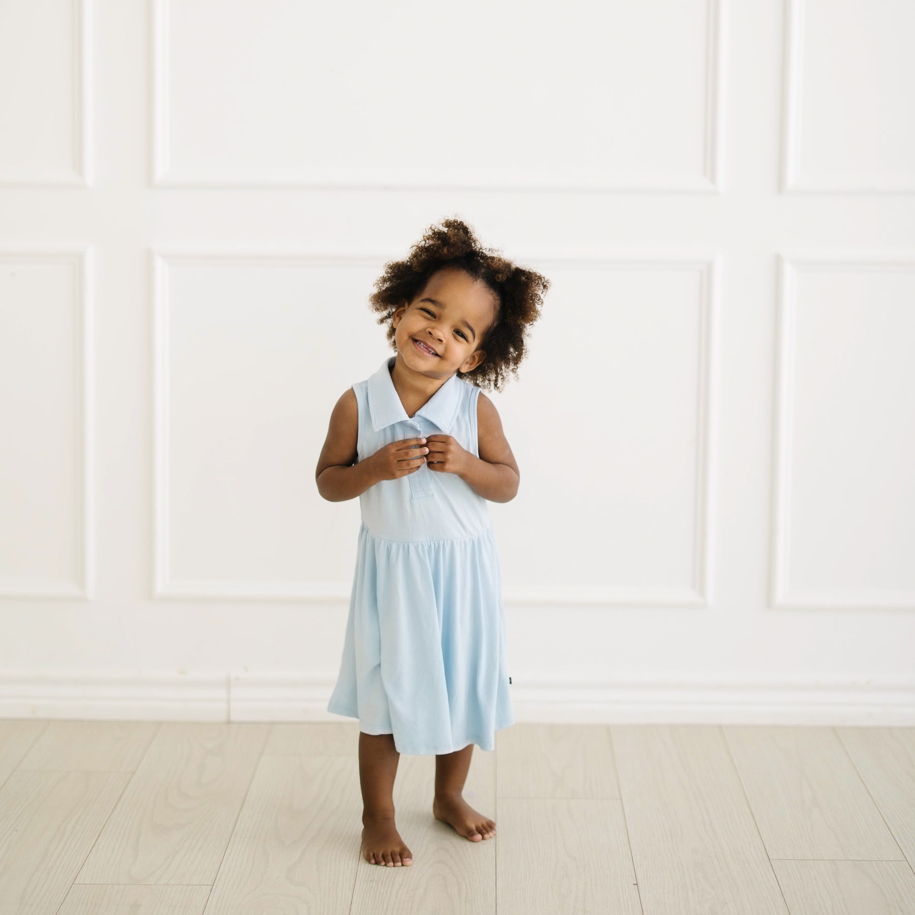 Young girl posing wearing the Polo Bodysuit Dress in Breeze standing in front of a white wall