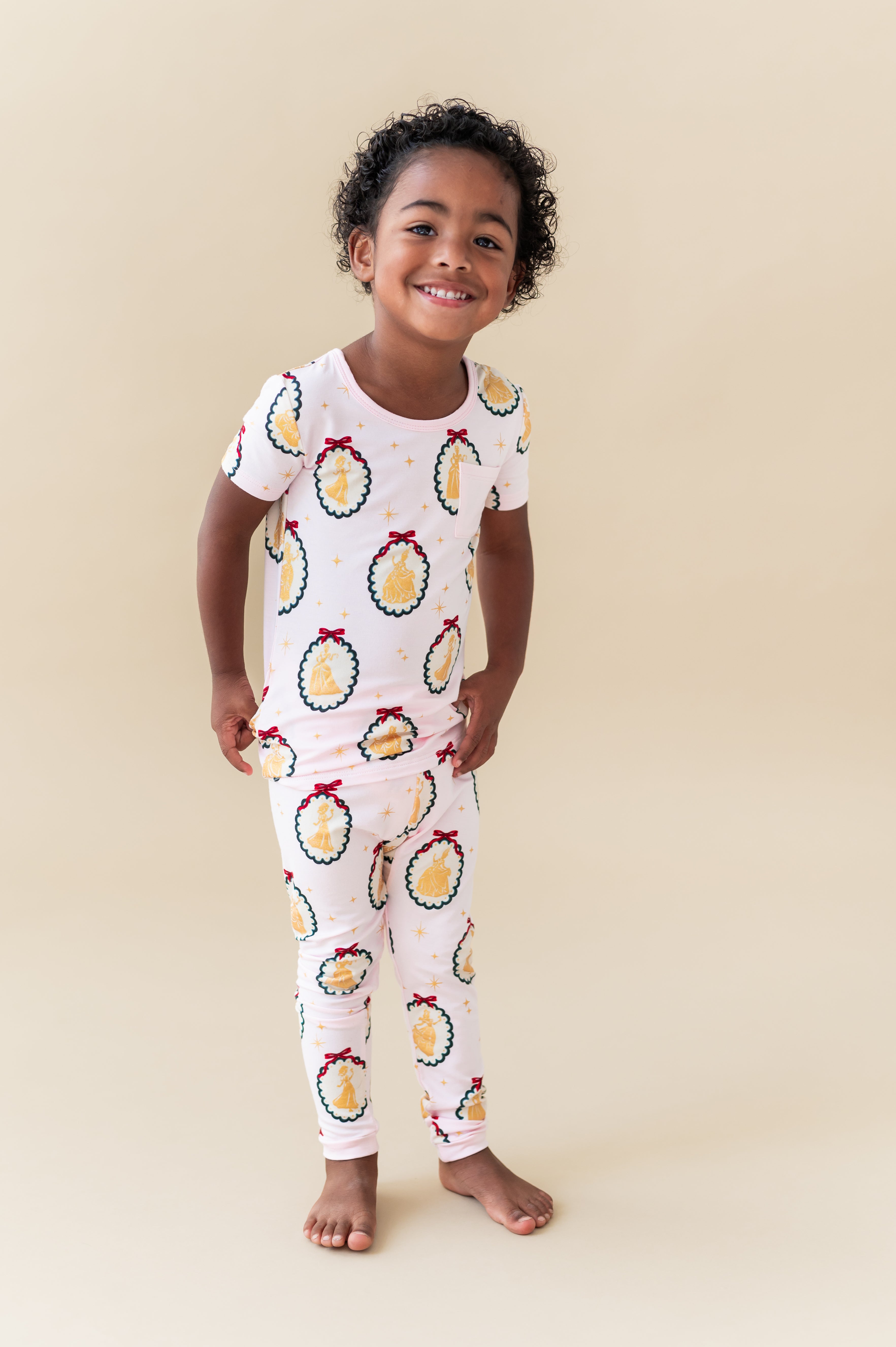 Child smiling in Short Sleeve with Pants Pajamas in Princess Holiday Portraits print on a beige background