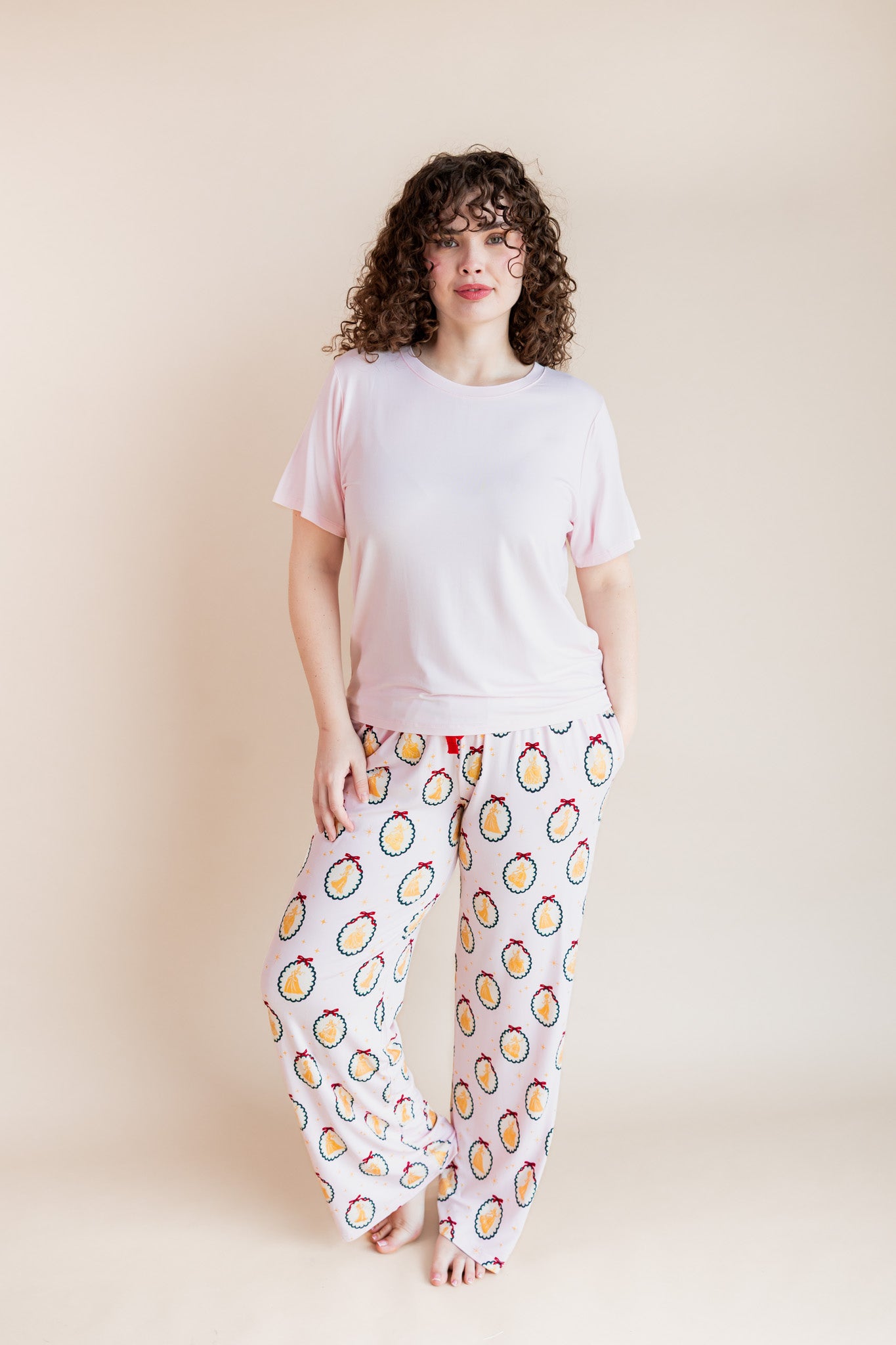 Woman wearing Women's Lounge Pants in Princess Holiday Portraits print under pink T-shirt on a beige background