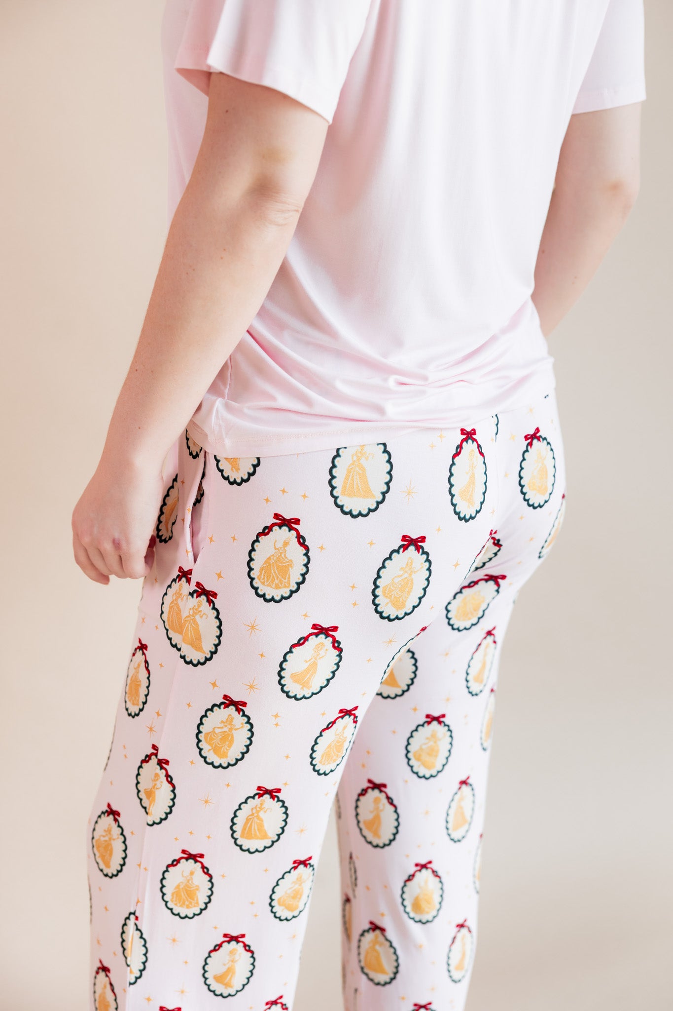 Back side of Modal wearing Women's Lounge Pants in Princess Holiday Portraits print under pink T-shirt on a beige background