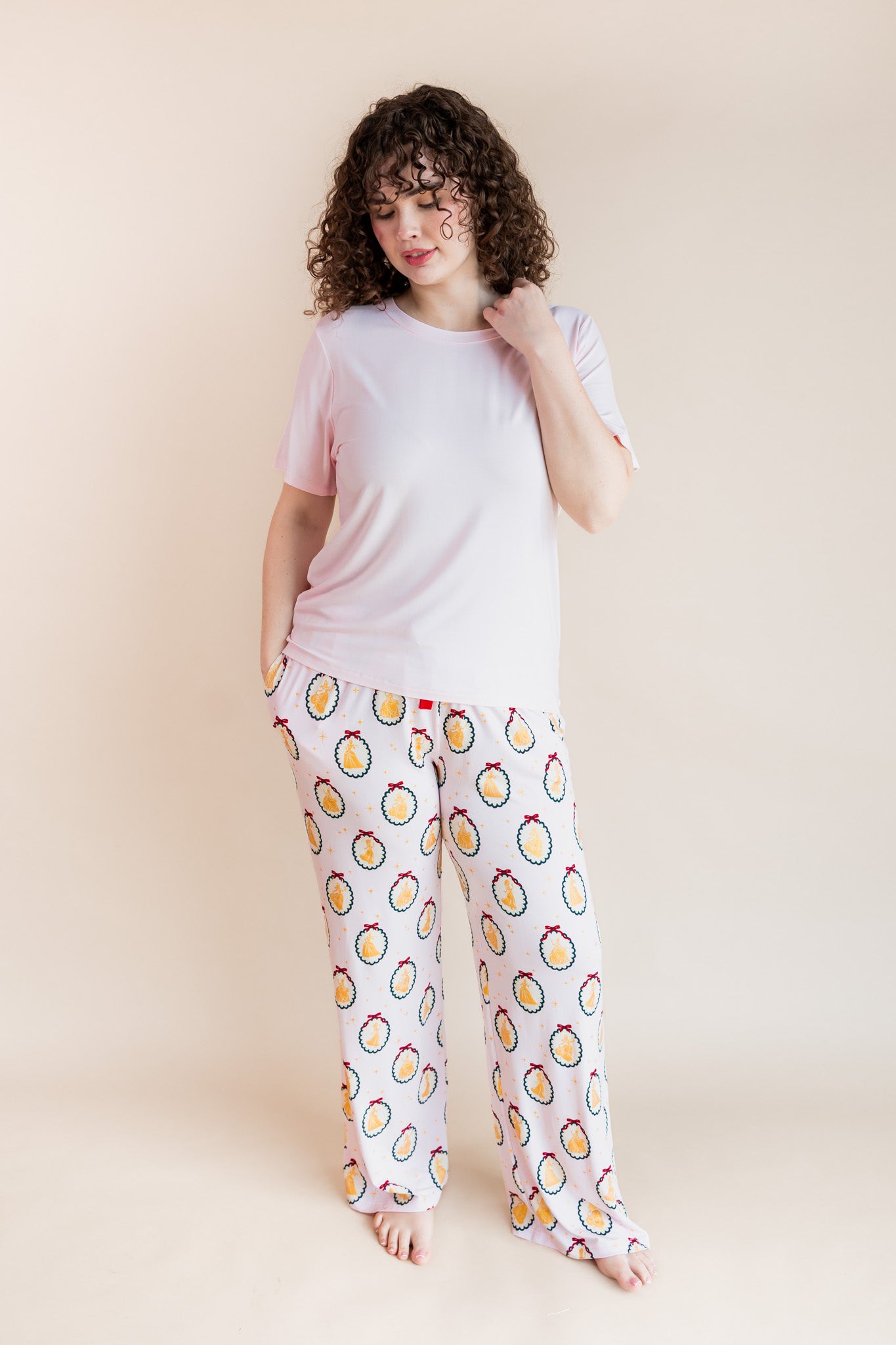 woman posing in Women's Lounge Pants in Princess Holiday Portraits print under pink T-shirt on a beige background