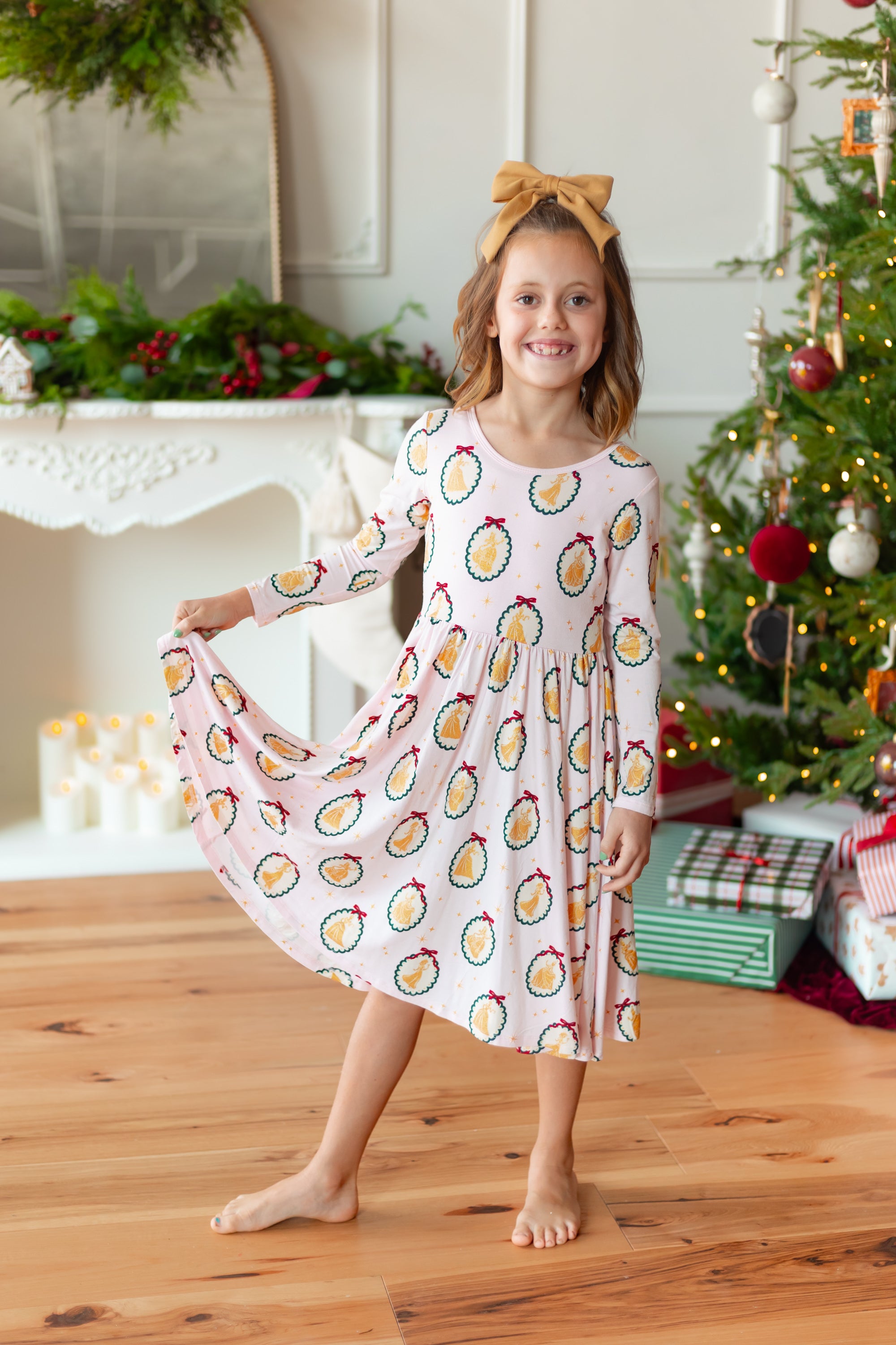 Girl smiling in Long Sleeve Twirl Dress in Princess Holiday Portraits print standing in front of Christmas tree and presents