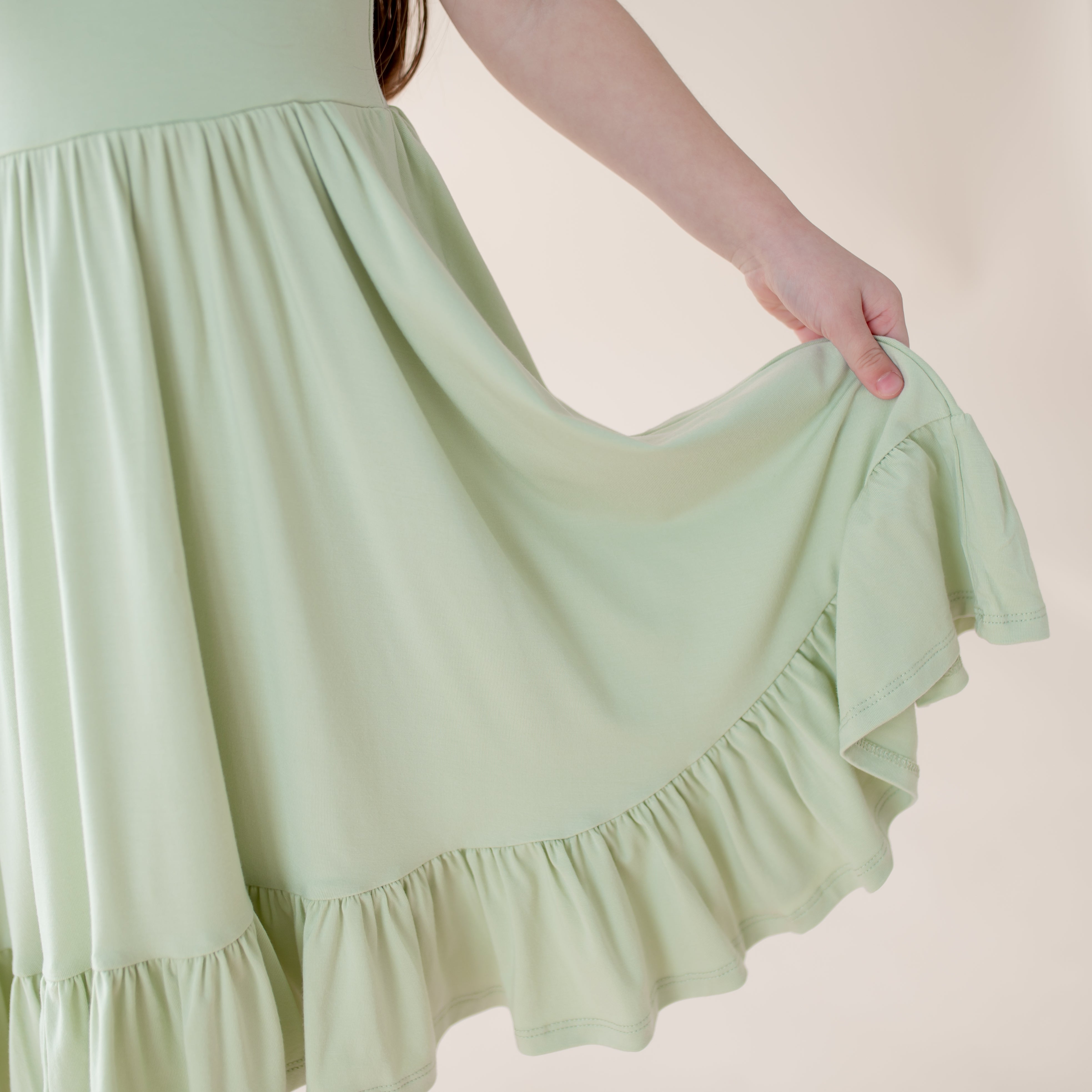 Light green dress with ruffled hem being held by a person against a plain background