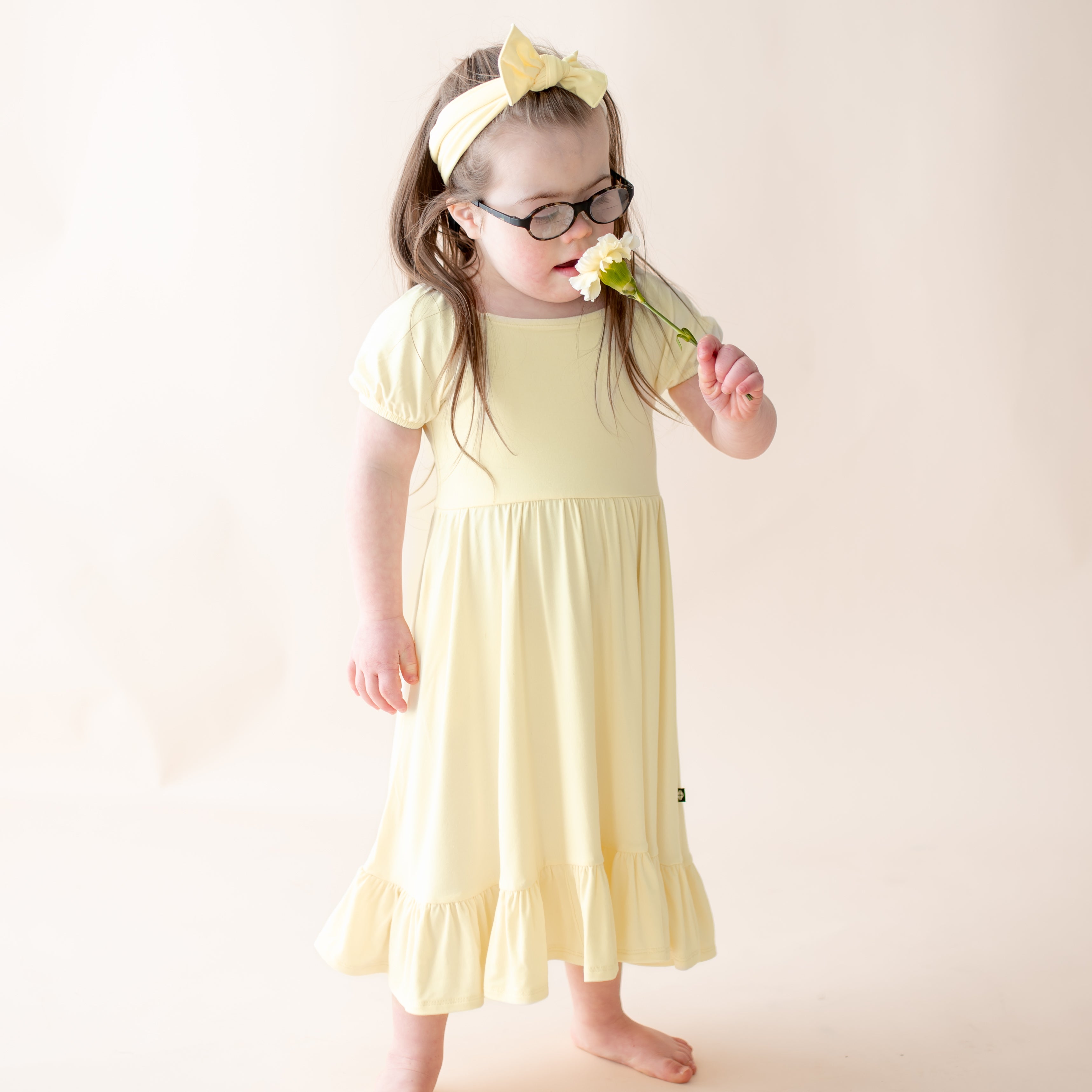 Toddler wearing a light yellow twirl dress with puff sleeves and a matching bow headband 