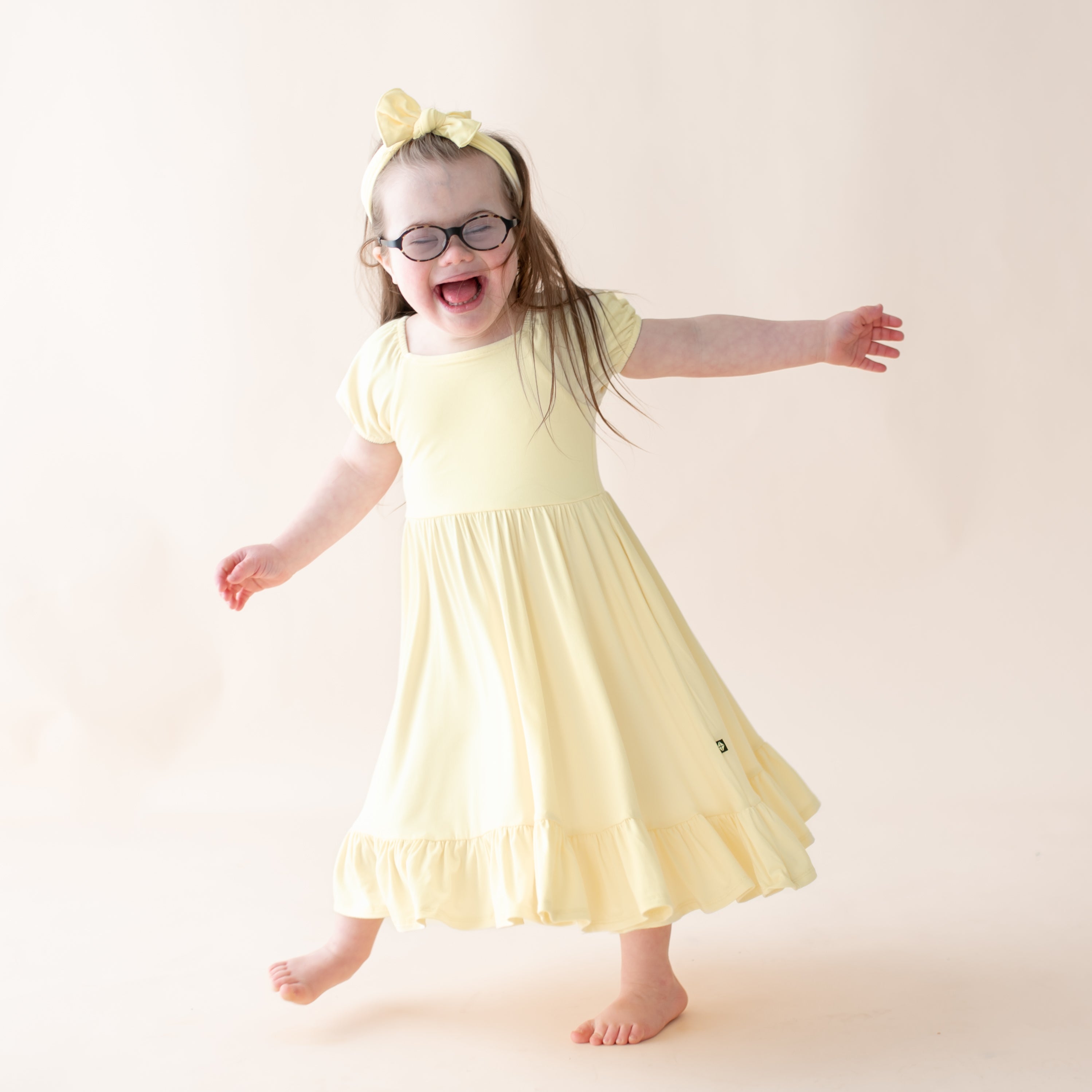 Child wearing a yellow dress and glasses on a plain background