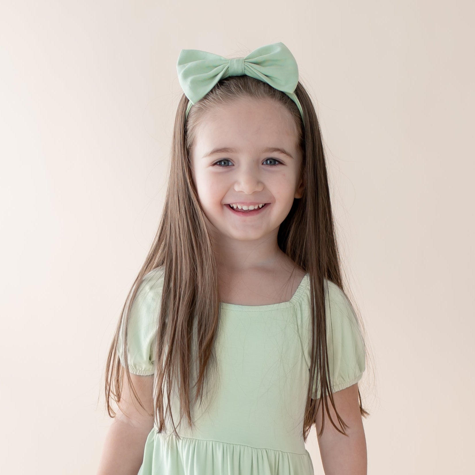 Young girl wearing the Bow Headband in Basil with a matching colored dress