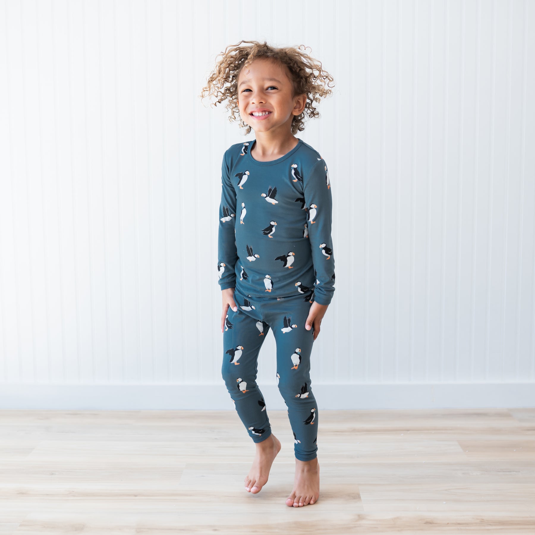 Young child jumping wearing the Long Sleeve Pajamas in Puffin in front of a white paneled wall