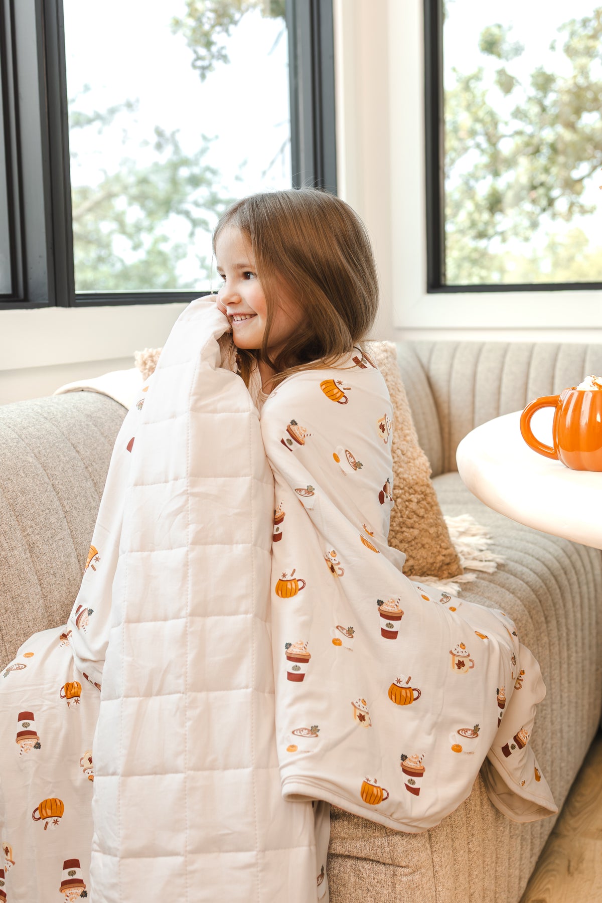 Girl sitting on a beige sofa wrapped in Youth Blanket with Pumpkin Spice Latte 2.5 print