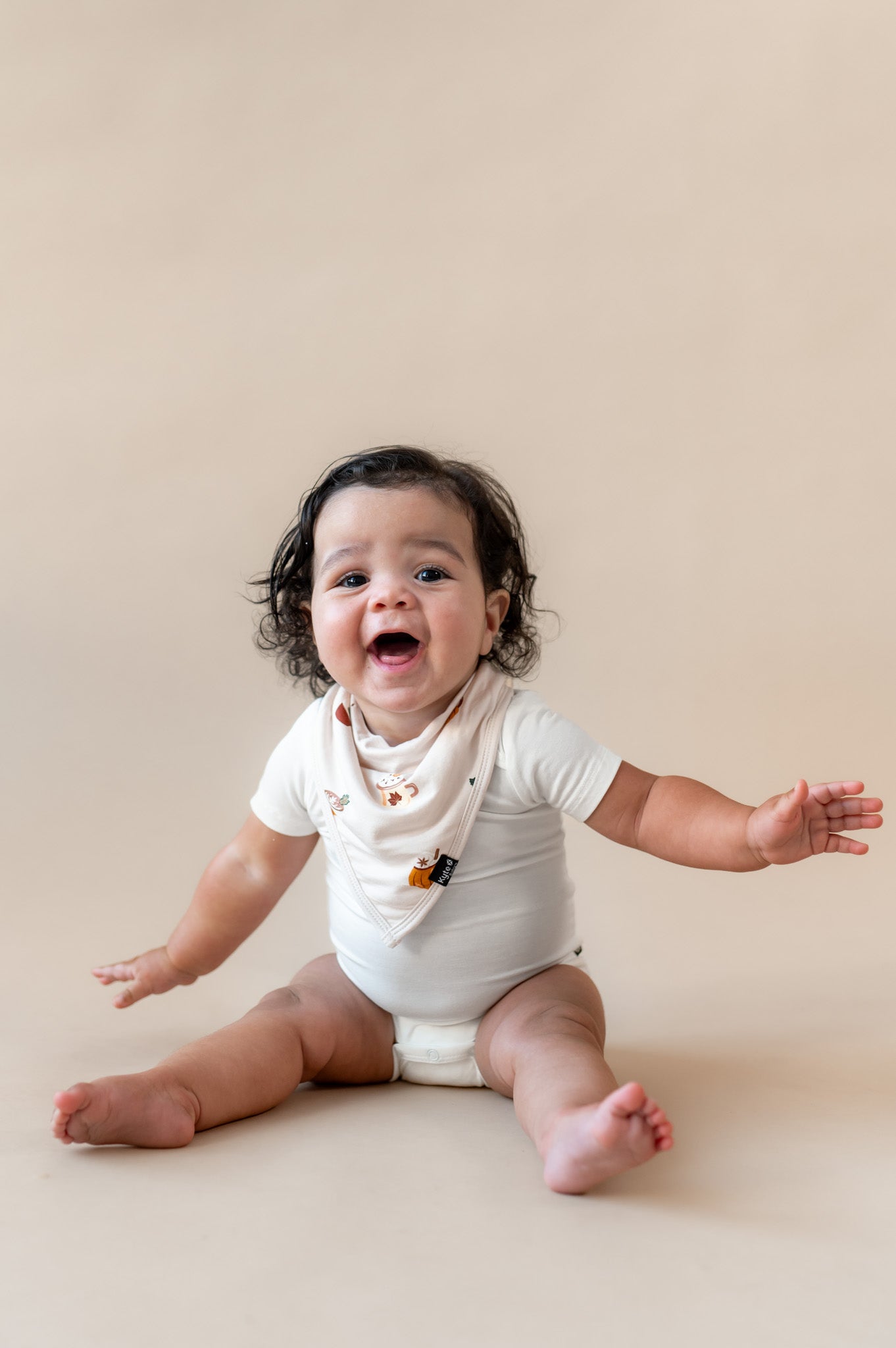 Baby wearing Bib with Pumpkin Spice Latte over white bodysuit on a beige background