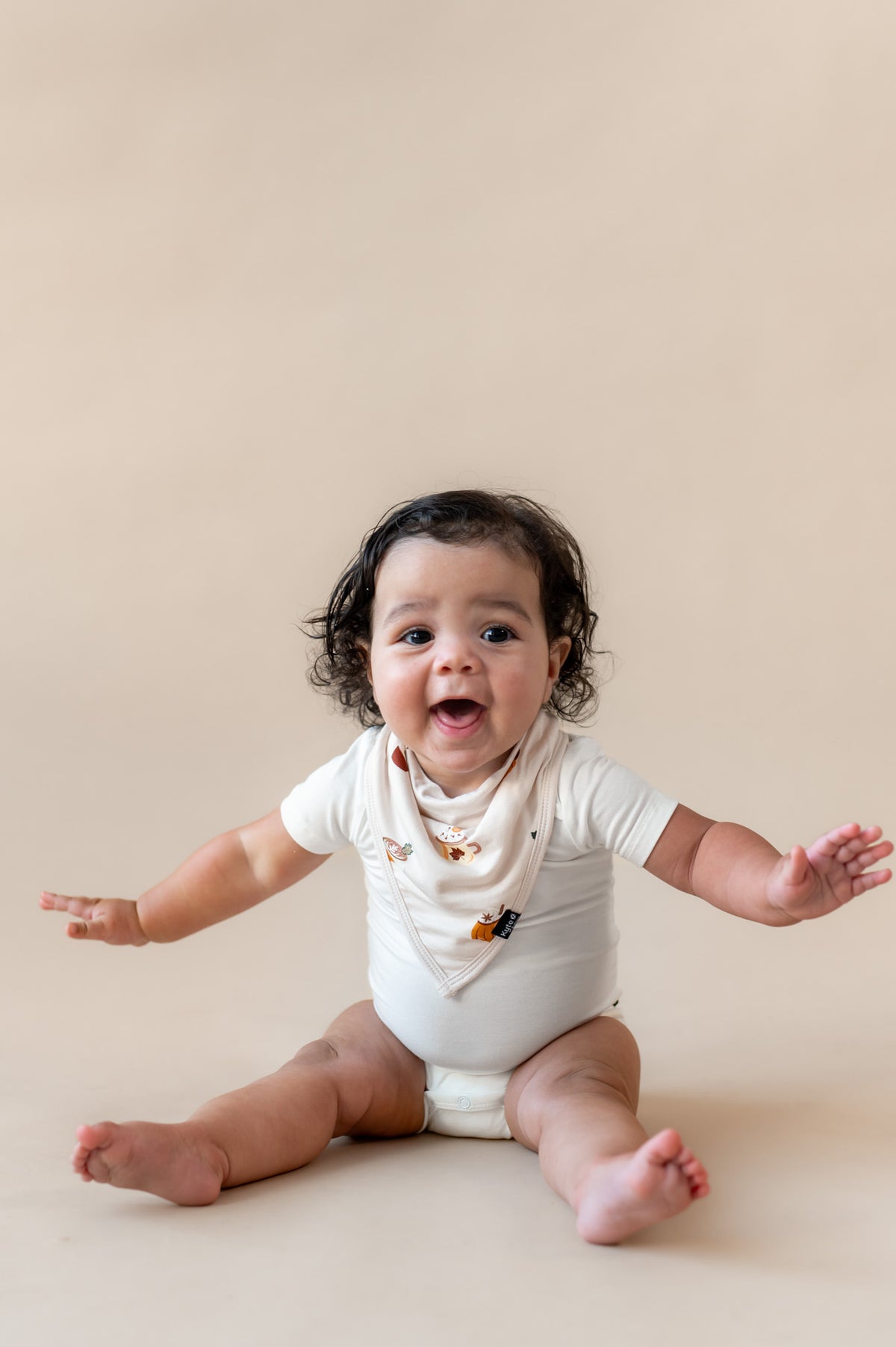 Baby posing wearing Bib with Pumpkin Spice Latte over white bodysuit on a beige background