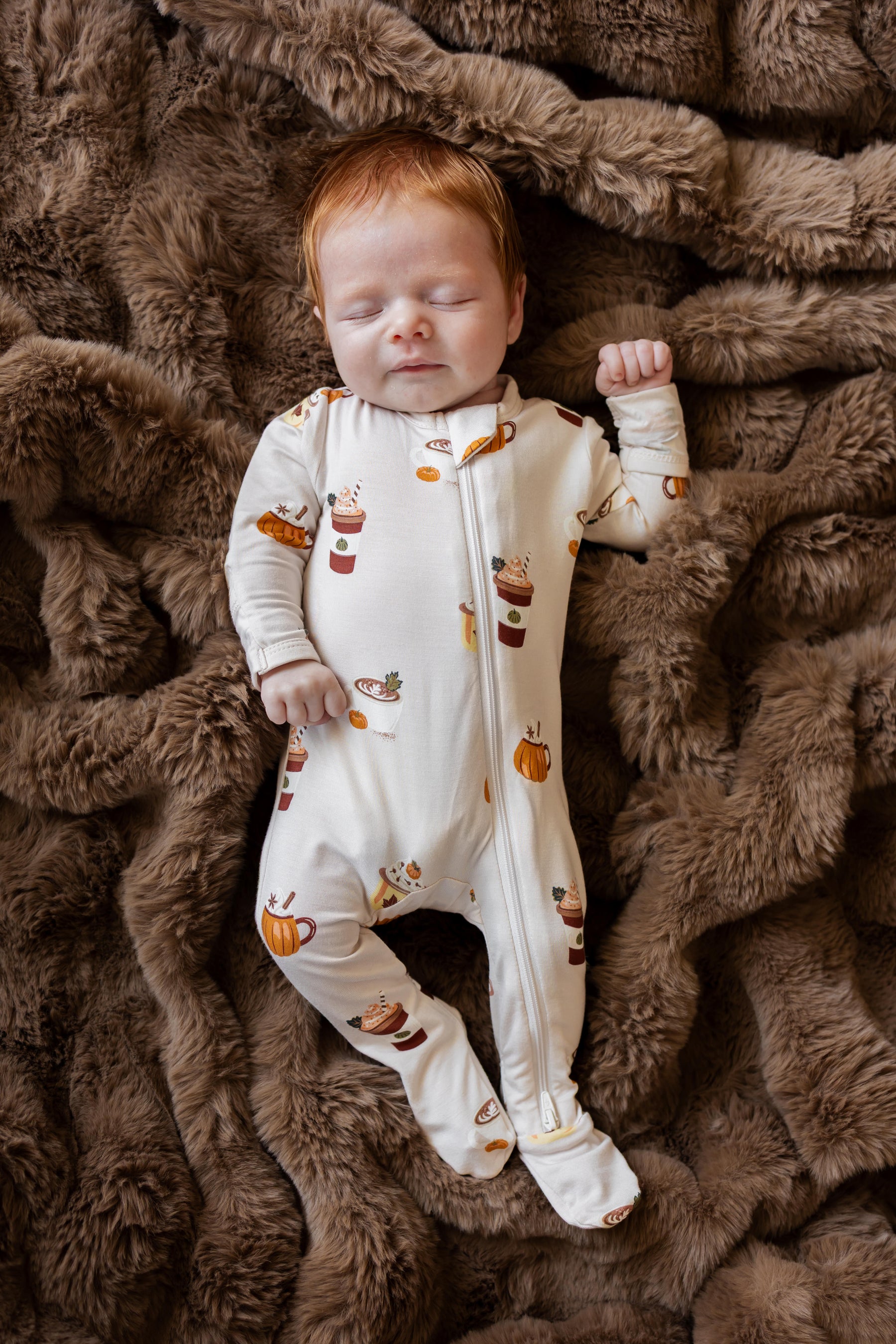 Baby wearing Zippered Footie with Pumpkin Spice Latte print sleeping on a brown fur blanket