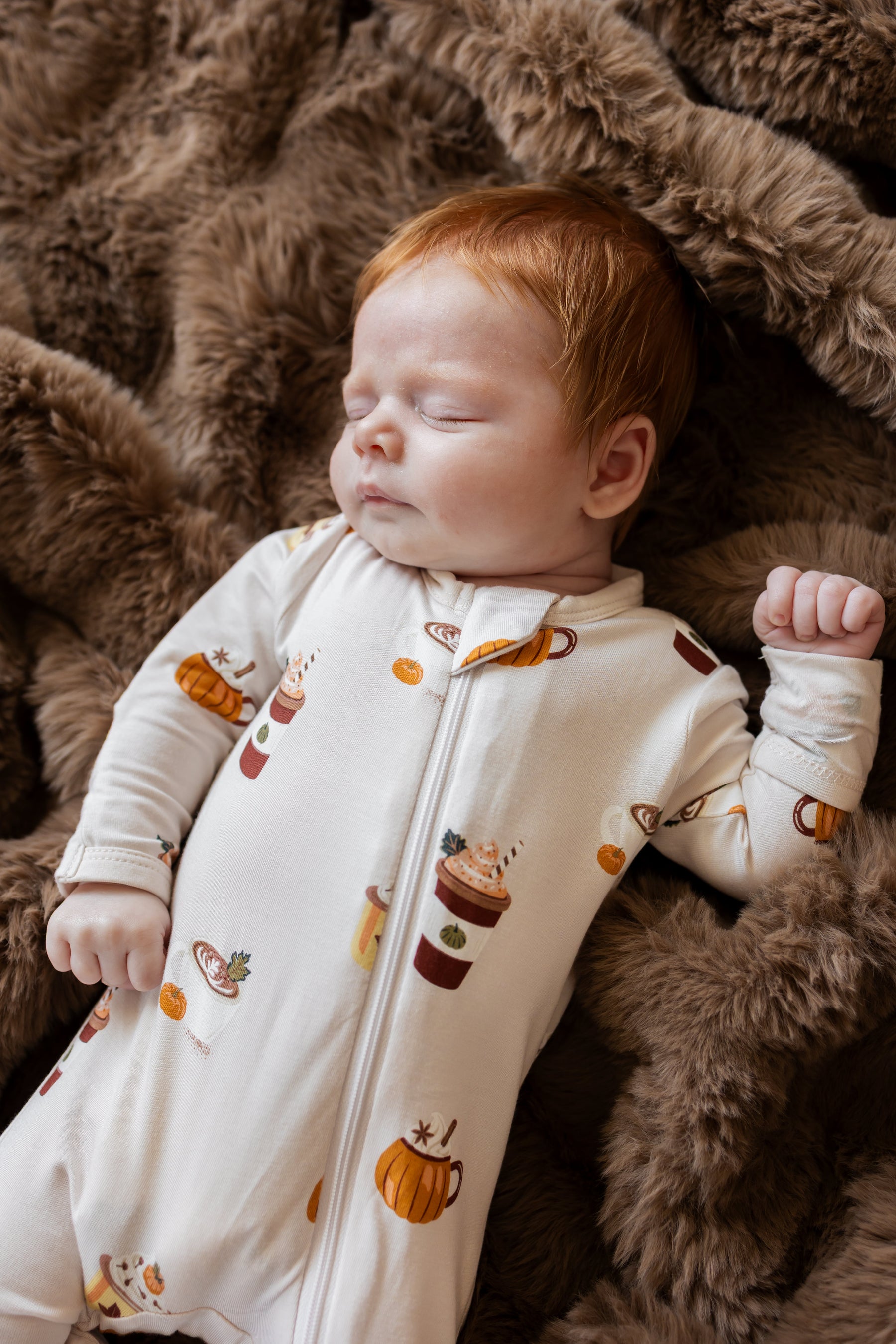 Close up of Baby wearing Zippered Footie with Pumpkin Spice Latte print  while sleeping on a brown fur blanket