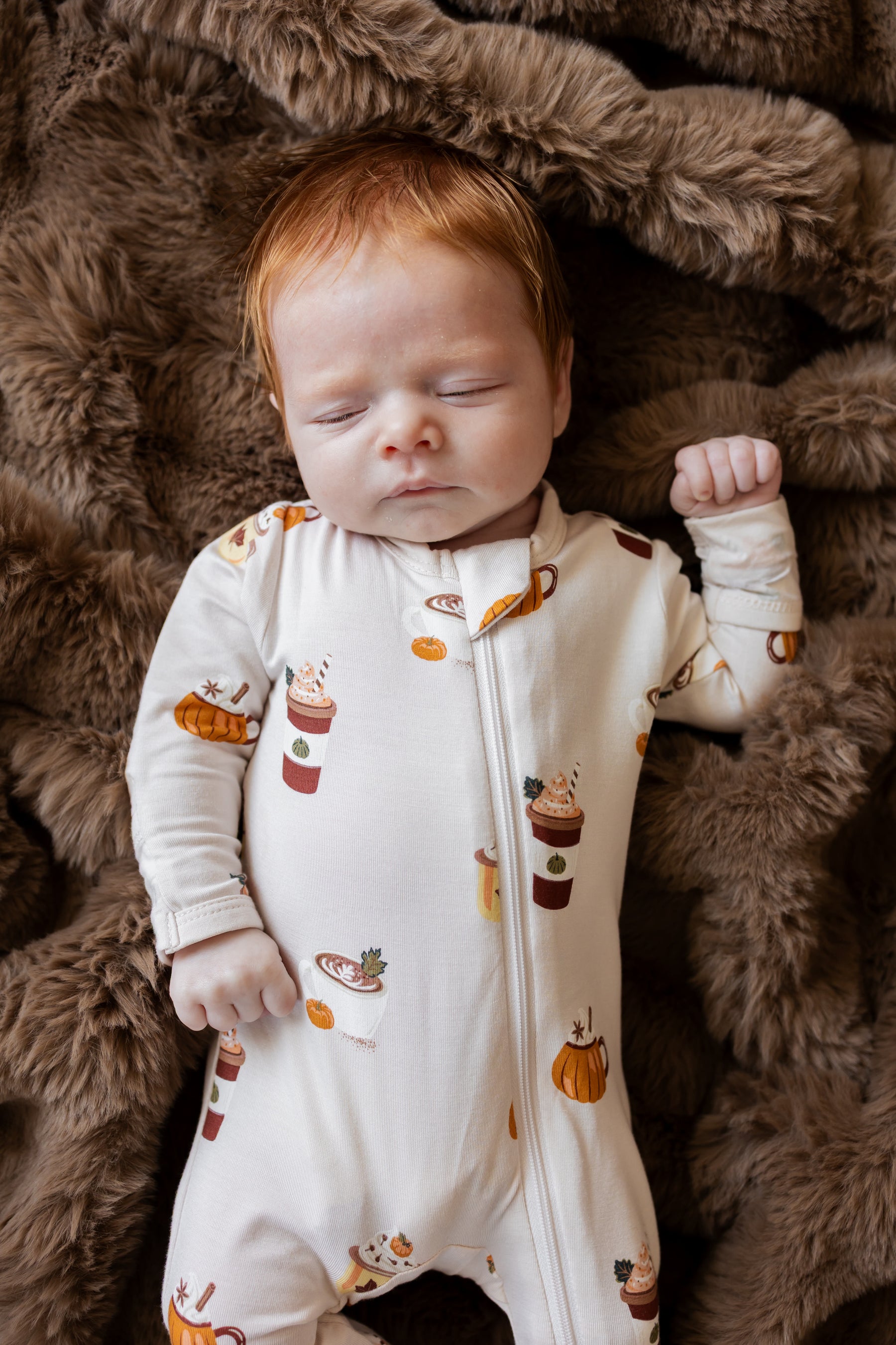 Baby sleeping in Zippered Footie with Pumpkin Spice Latte print on a brown fur blanket