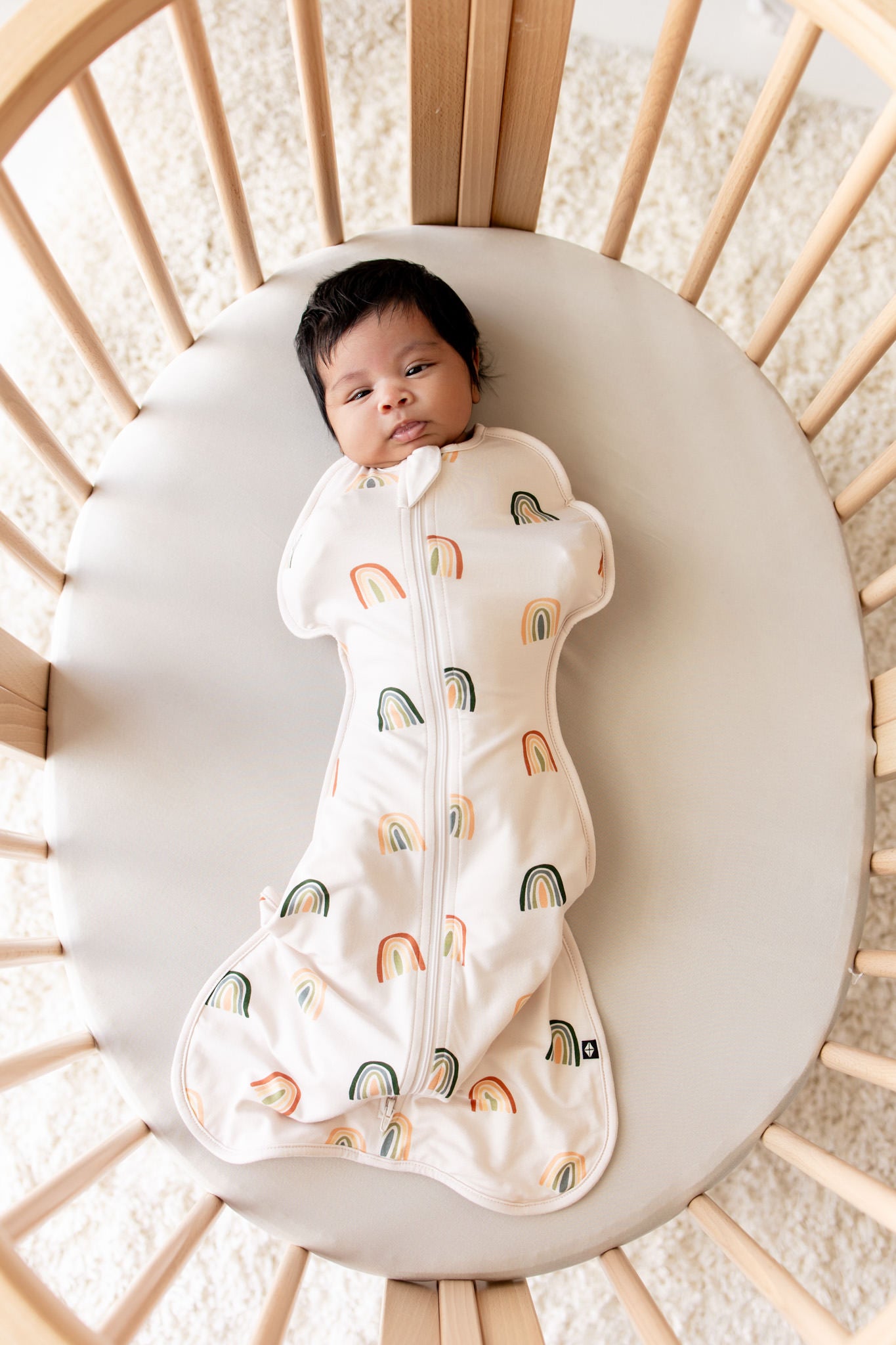 Baby lying in crib wearing Swaddle Bag in Retro Rainbow 0.5 print