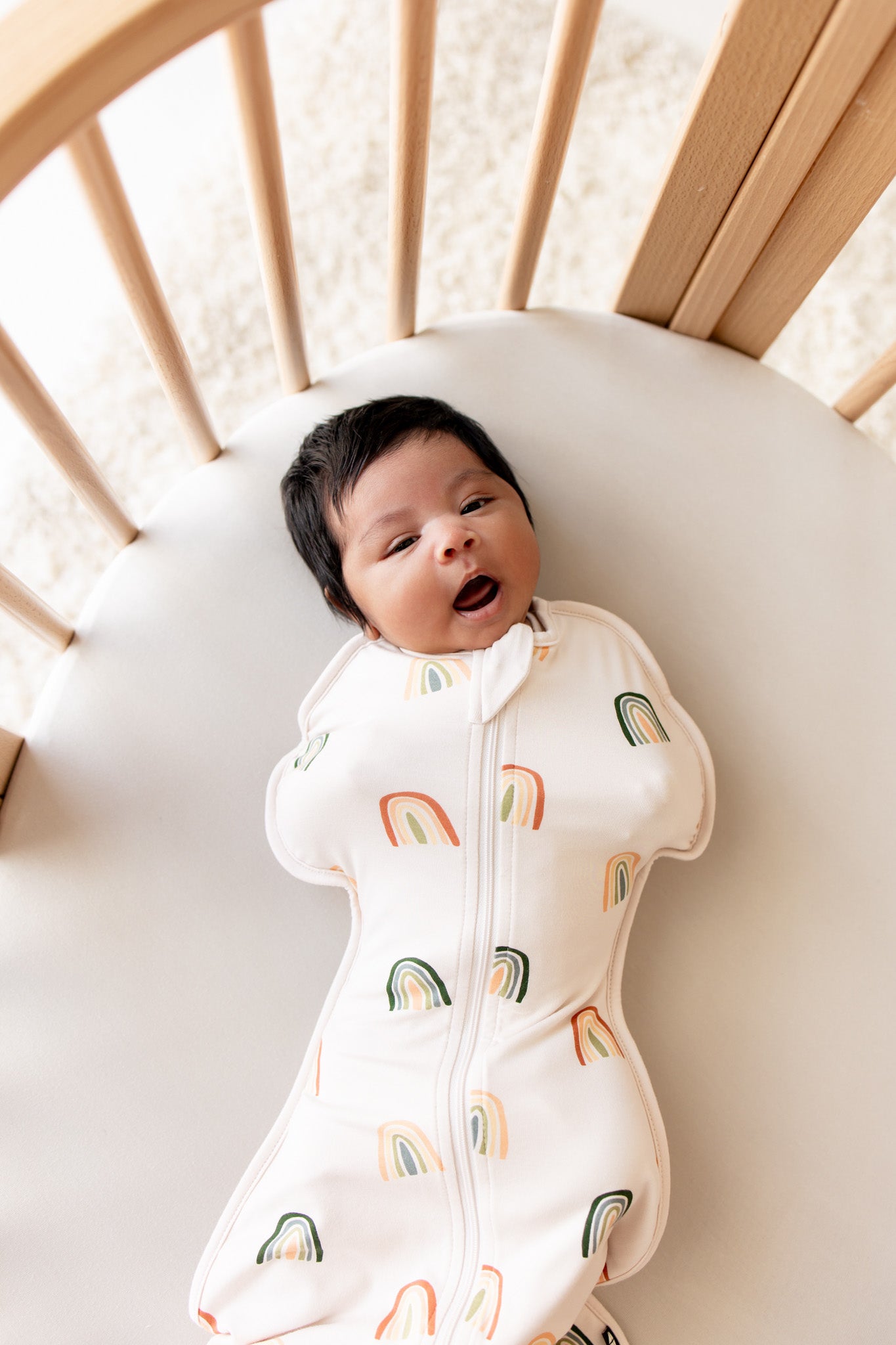 Baby yawning in crib wearing Swaddle Bag in Retro Rainbow 0.5 print