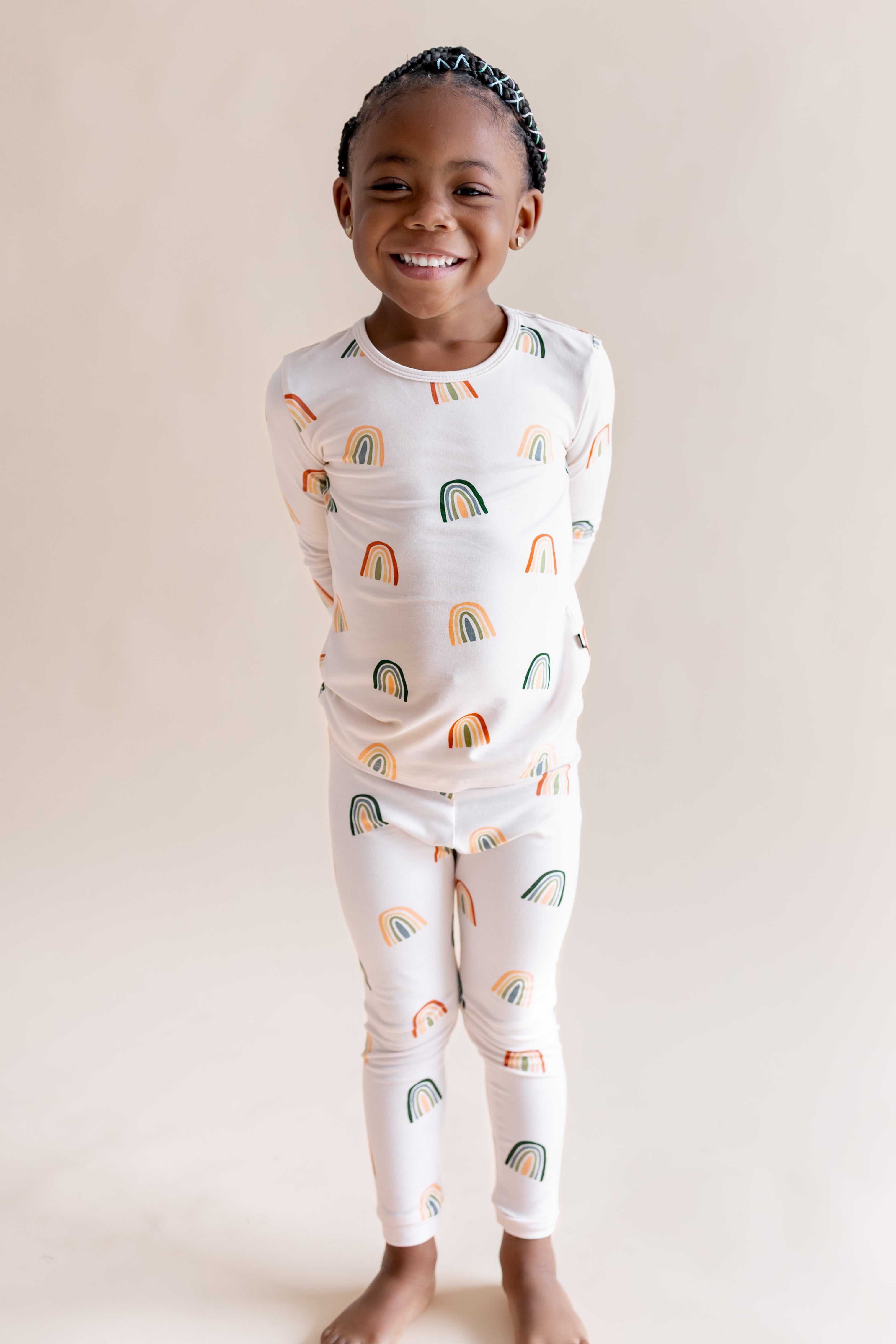 Toddler wearing Long Sleeve Pajamas in Retro Rainbow print on a beige background
