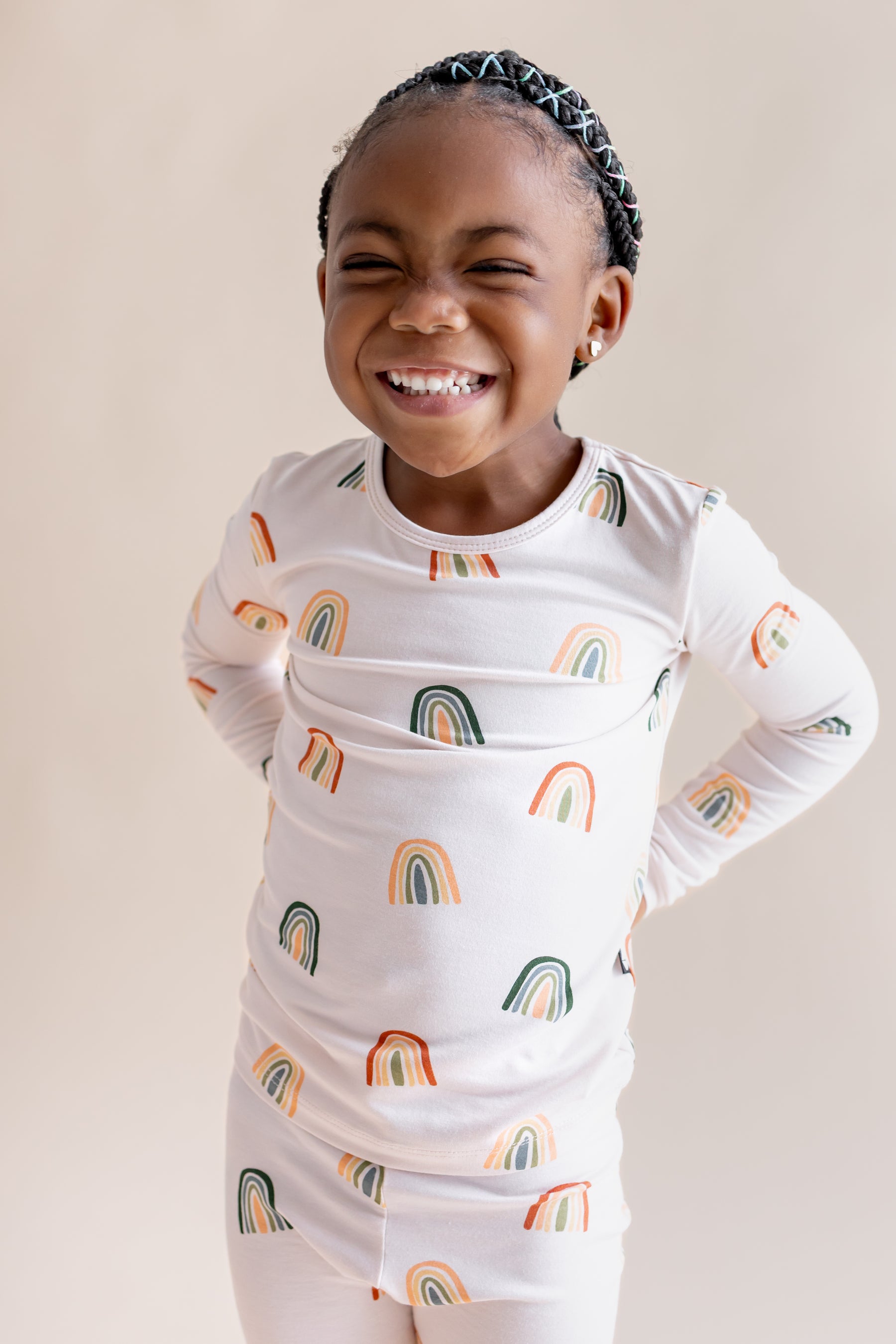 Girl smiling in Long Sleeve Pajamas in Retro Rainbow print on a beige background