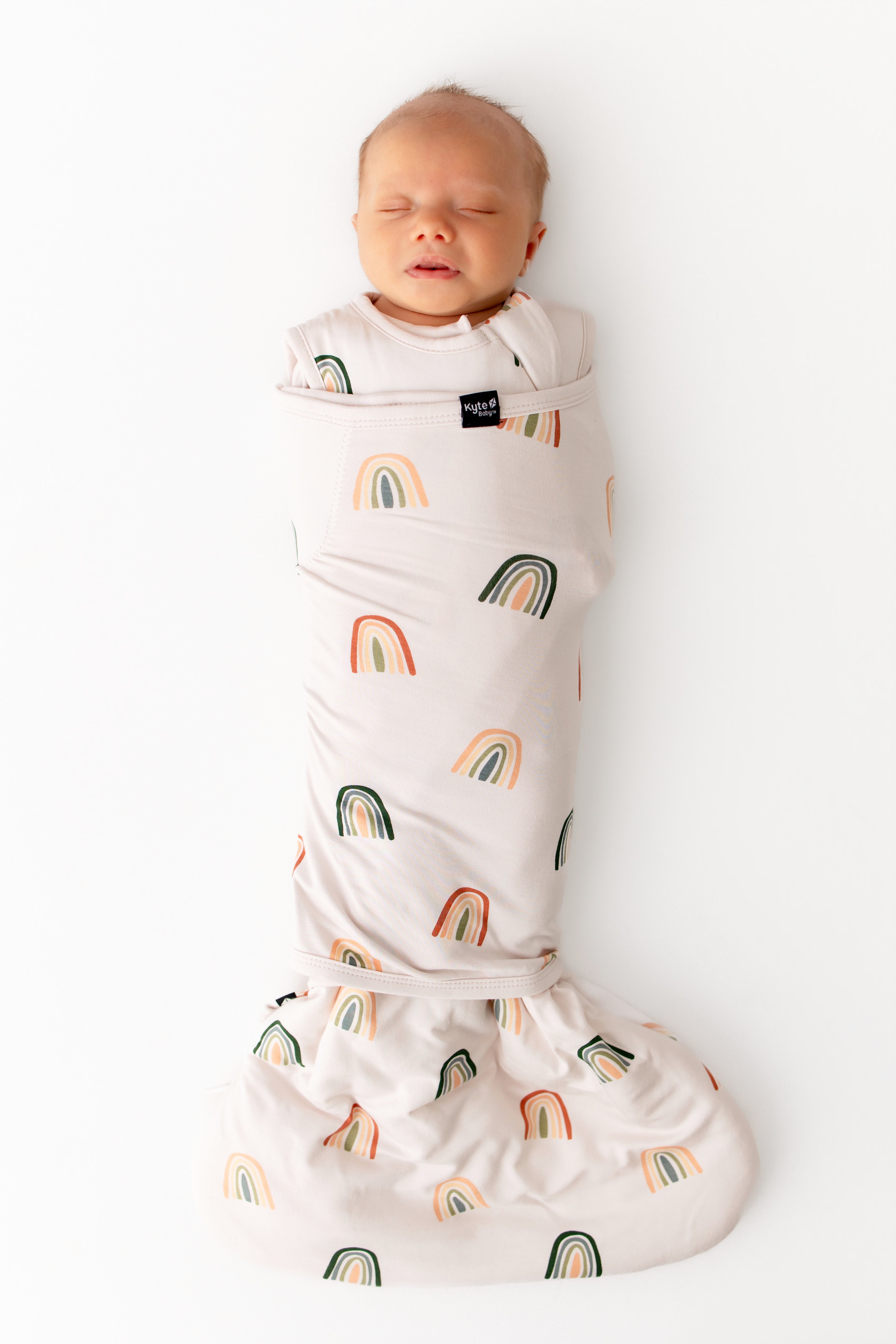 Baby sleeping in Sleep Bag Swaddler in Retro Rainbow 1.0 print on a white background